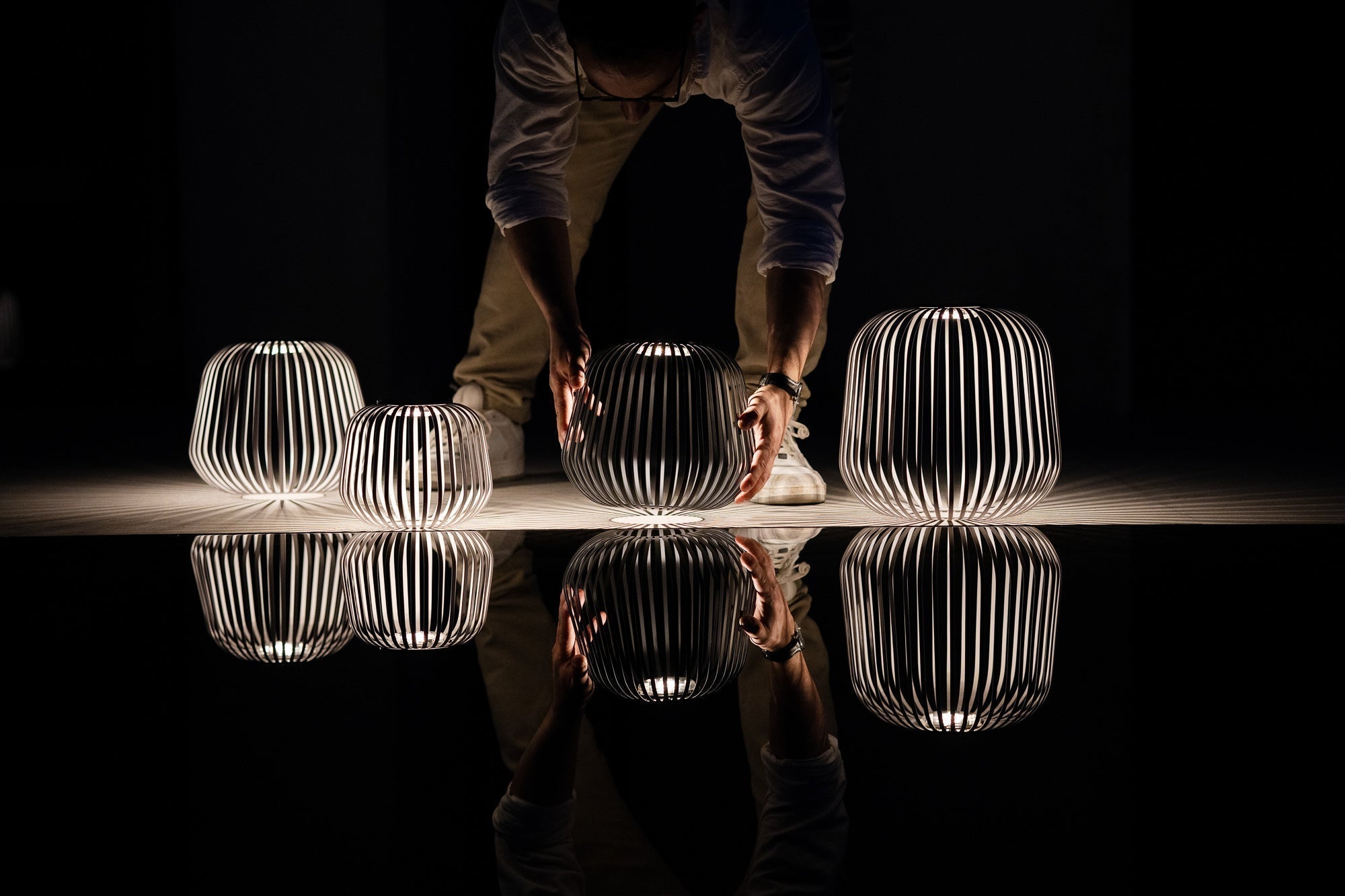 Mehrere beleuchtete Solarlaternen Solis werden auf einer reflektierenden Fläche arrangiert – eindrucksvolle Inszenierung mit Lichtreflexion und Schattenmuster, ideal für Designpräsentationen und stimmungsvolle Lichtinstallationen.