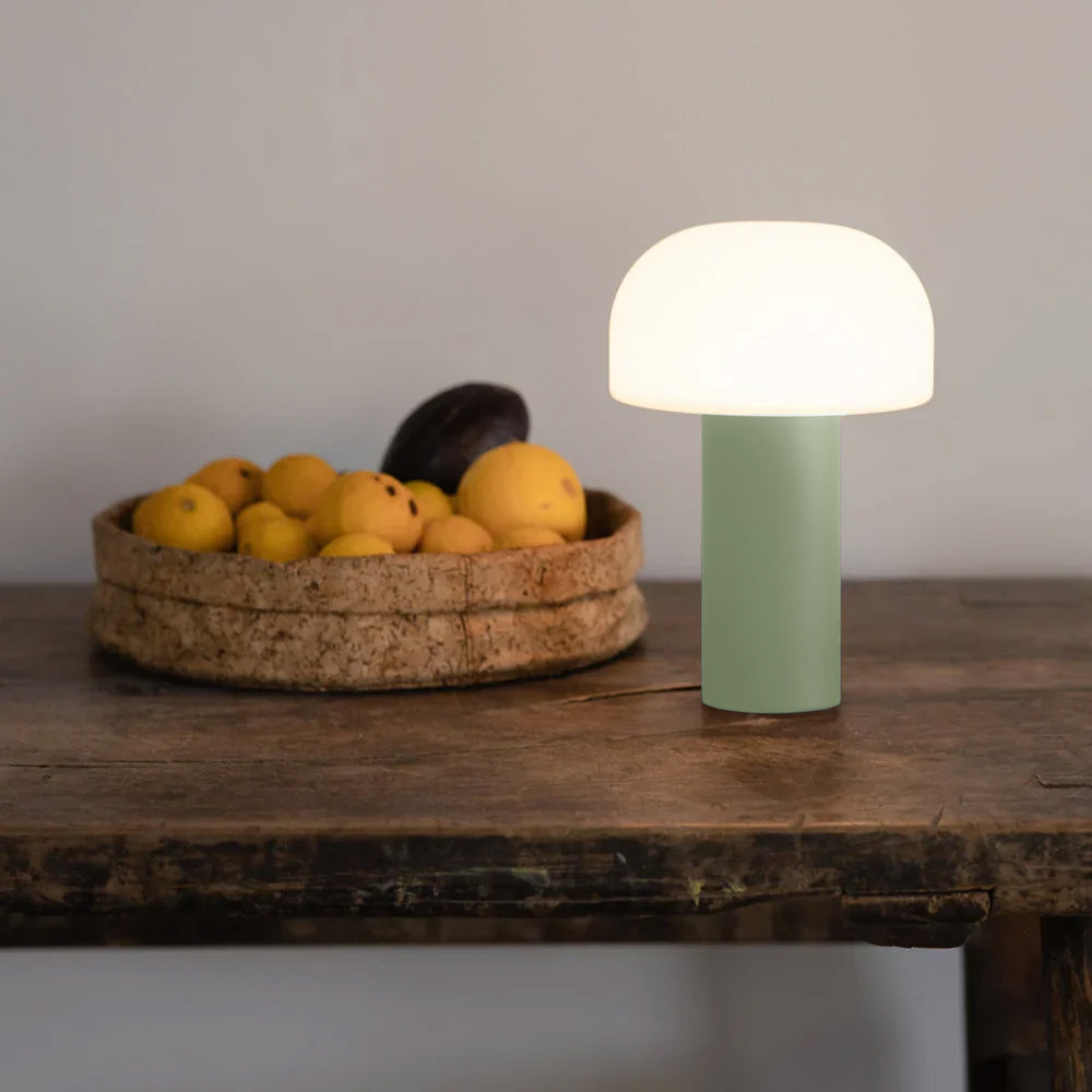 Ein Moodbild der kabellosen, Akkubetriebenen NOA Tischlampe von LUUK Studio in gruen auf einem hochwertigen Vollholz Tisch