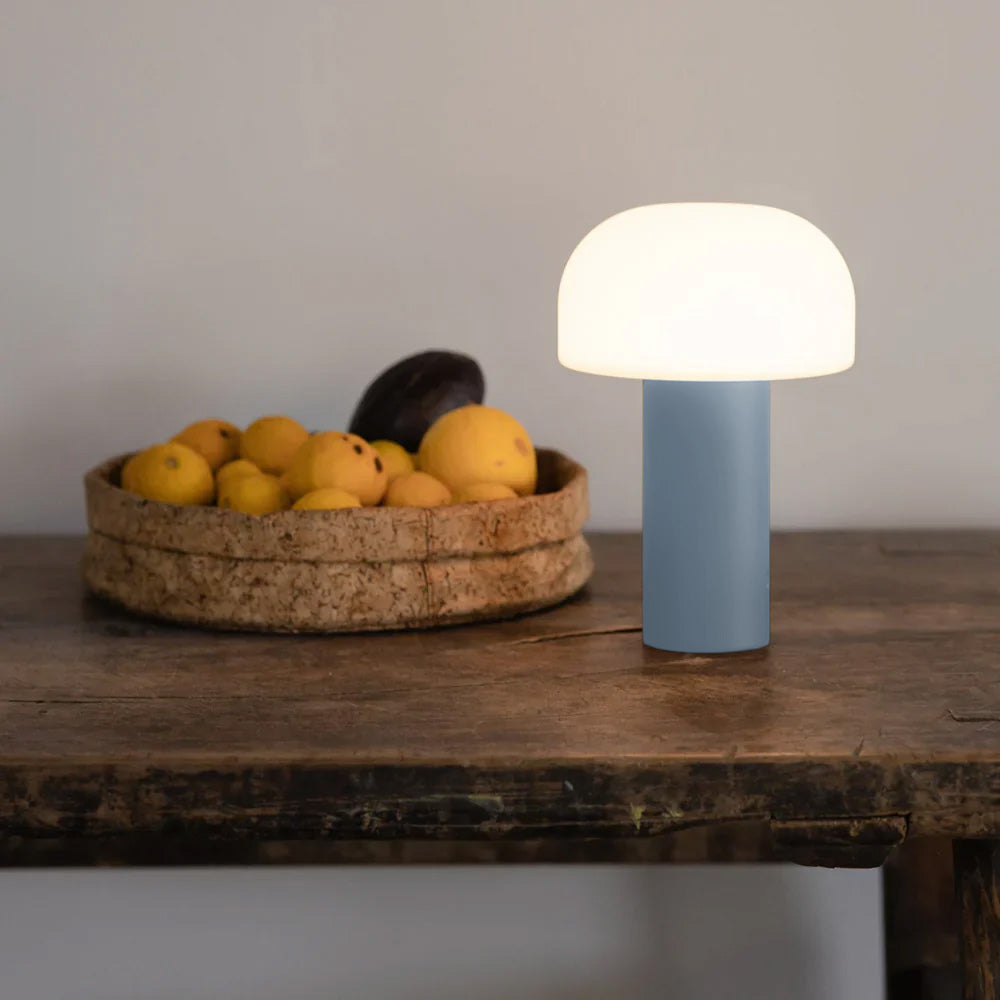 Leuchtende, LED Tischlampe von LUUK Studio aus der NOA Kollektion in der Farbe hellblau auf Holztisch mit Obstkorb in dem Zitronen liegen