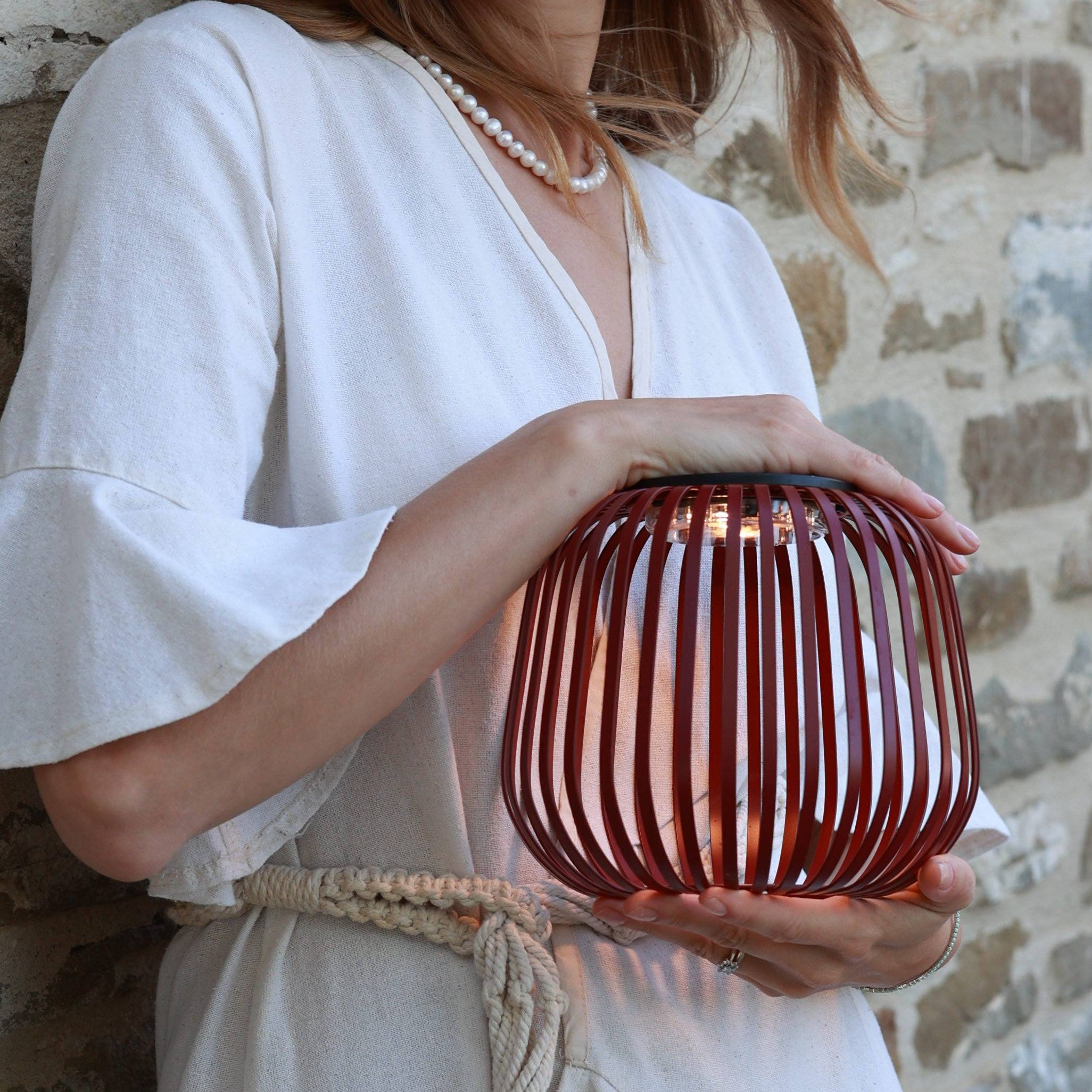 Dekorative Solarlaterne von LUUK Studio mit Metzallstreben in rot wird von Frau im Sommerkleid in der Hand gehalten