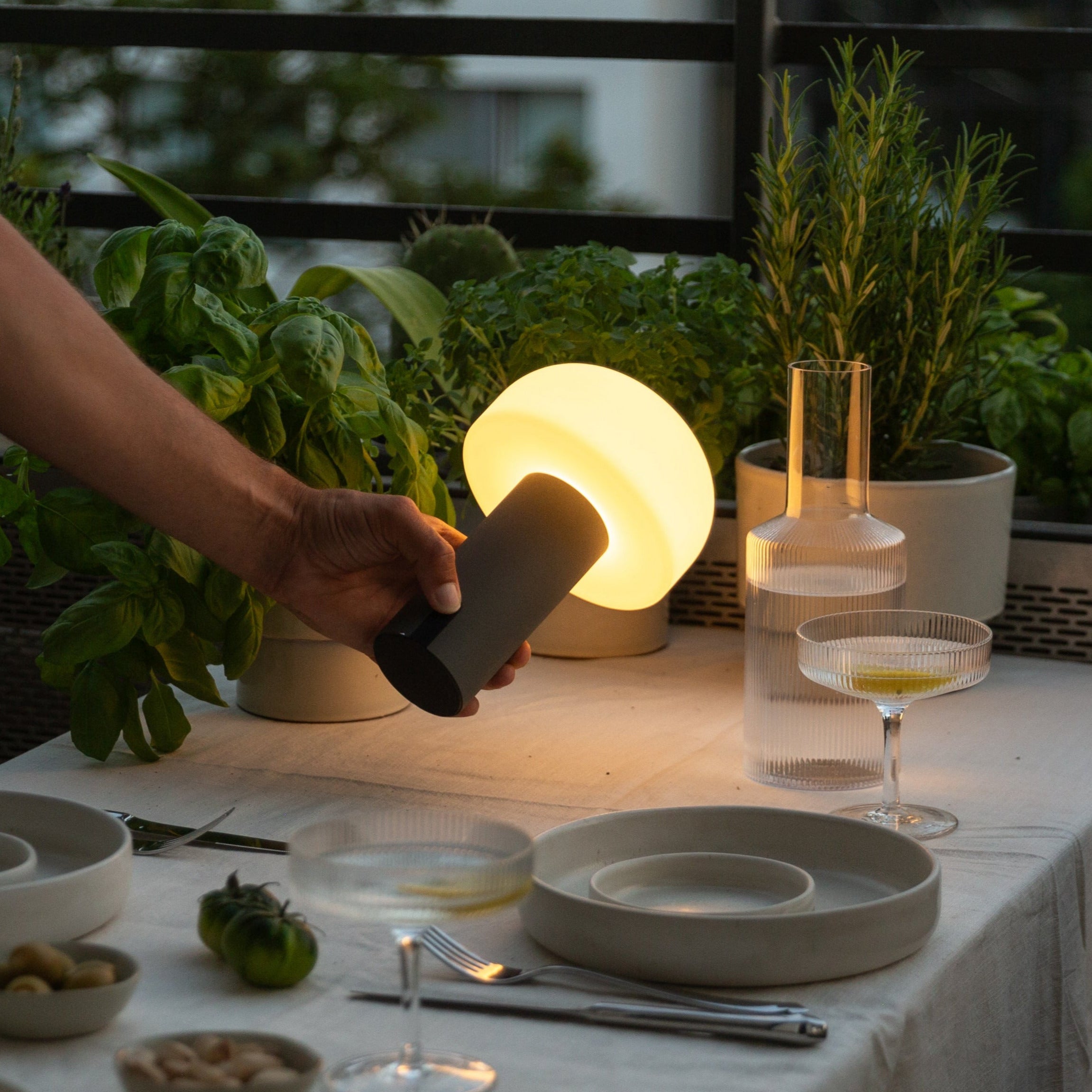 Stufenlos dimmbare LED-Tischleuchte von LUUK Studio in Schwarz – kabellos und mobil, im Einsatz beim Abendessen auf dem Balkon