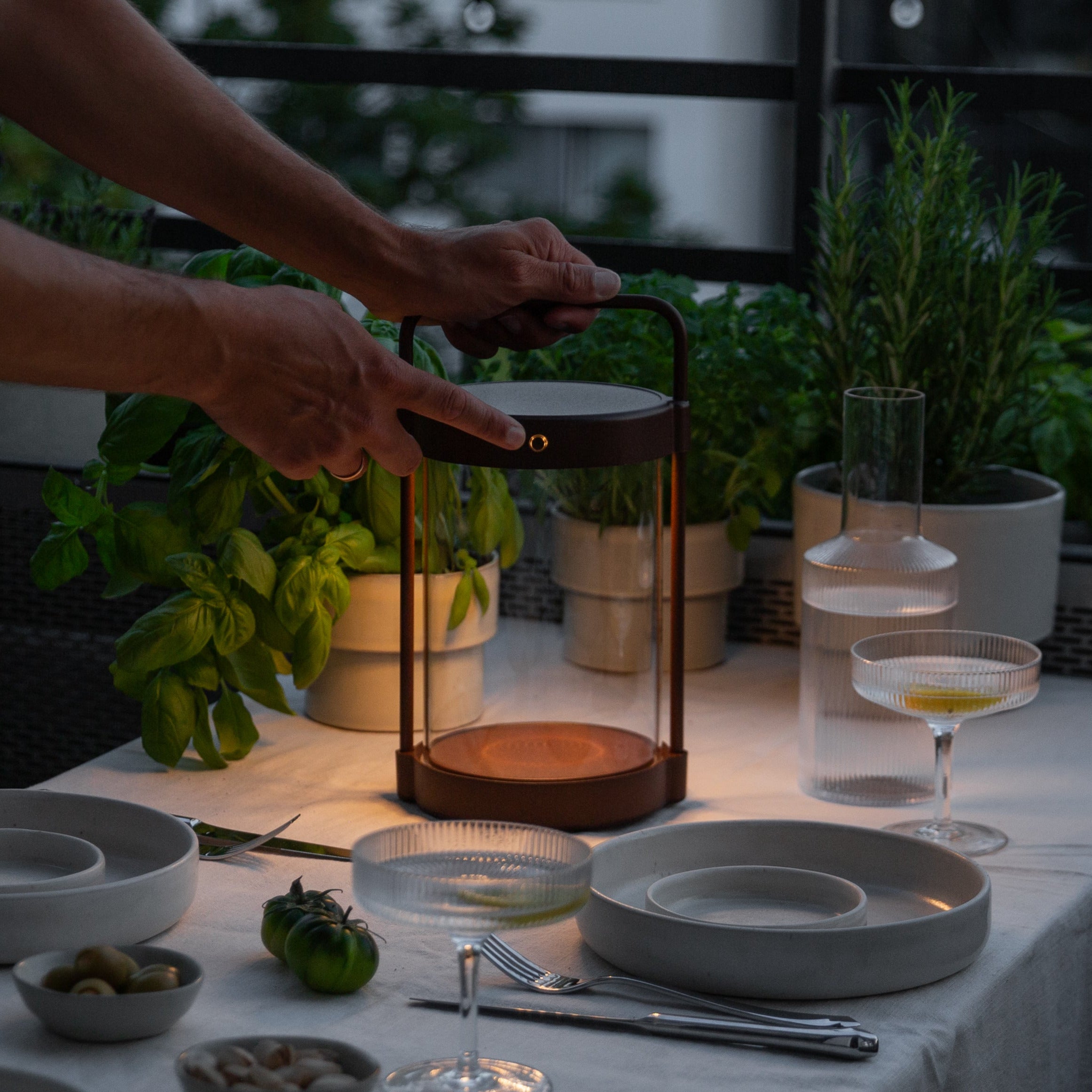Dimmbare Caia Solarlaterne in Braun mit Echtglas beim Einsatz auf gedecktem Balkontisch – stimmungsvolle, kabellose LED-Außenbeleuchtung bei Abenddämmerung