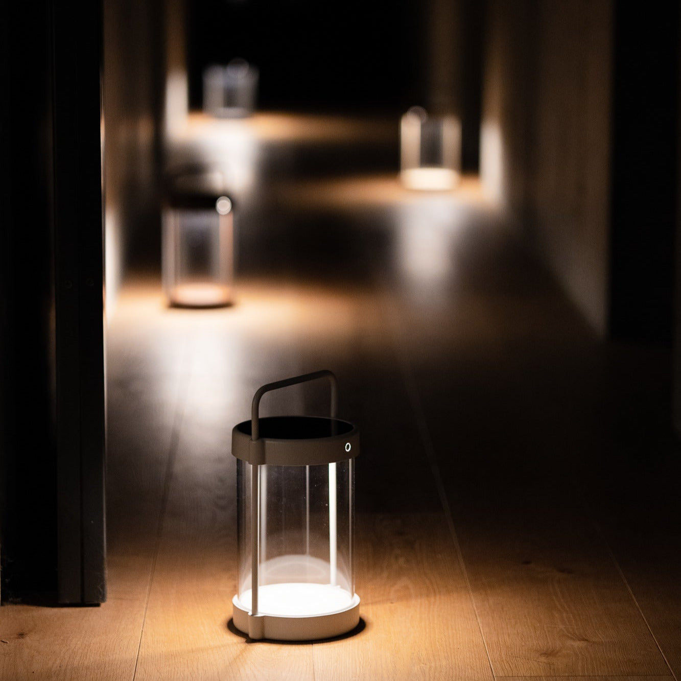 Mehrere dimmbare Caia Solarlaternen von Luuk Studio spenden stimmungsvolles, indirektes Licht entlang eines dunklen Flurs – stilvolle mobile Nachtbeleuchtung ohne Kabel