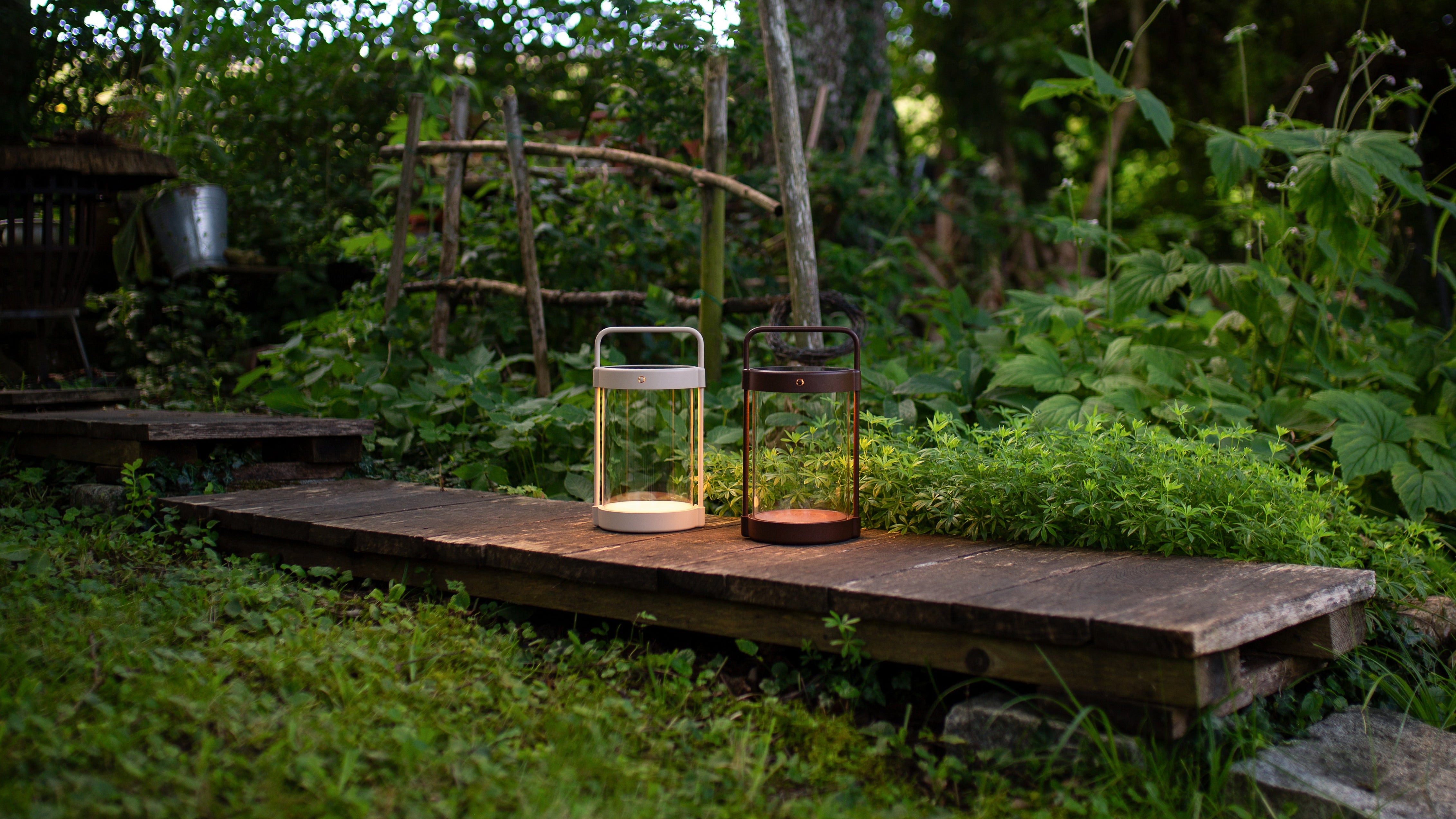 LED Design-Solarlaternen Caia von LUUK Studio auf Holzsteg im grünen Garten, beige und braun leuchtend bei Sonnenuntergang