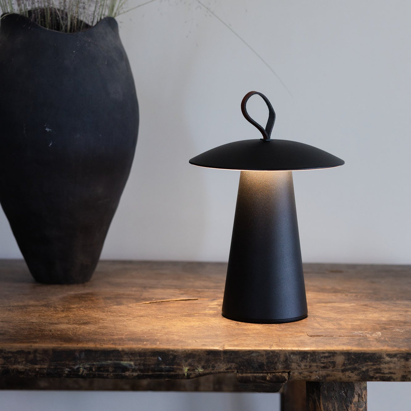 Stufenlos dimmbare LED-Tischleuchte von LUUK Studio in Weiß auf Holztisch mit Naturdeko