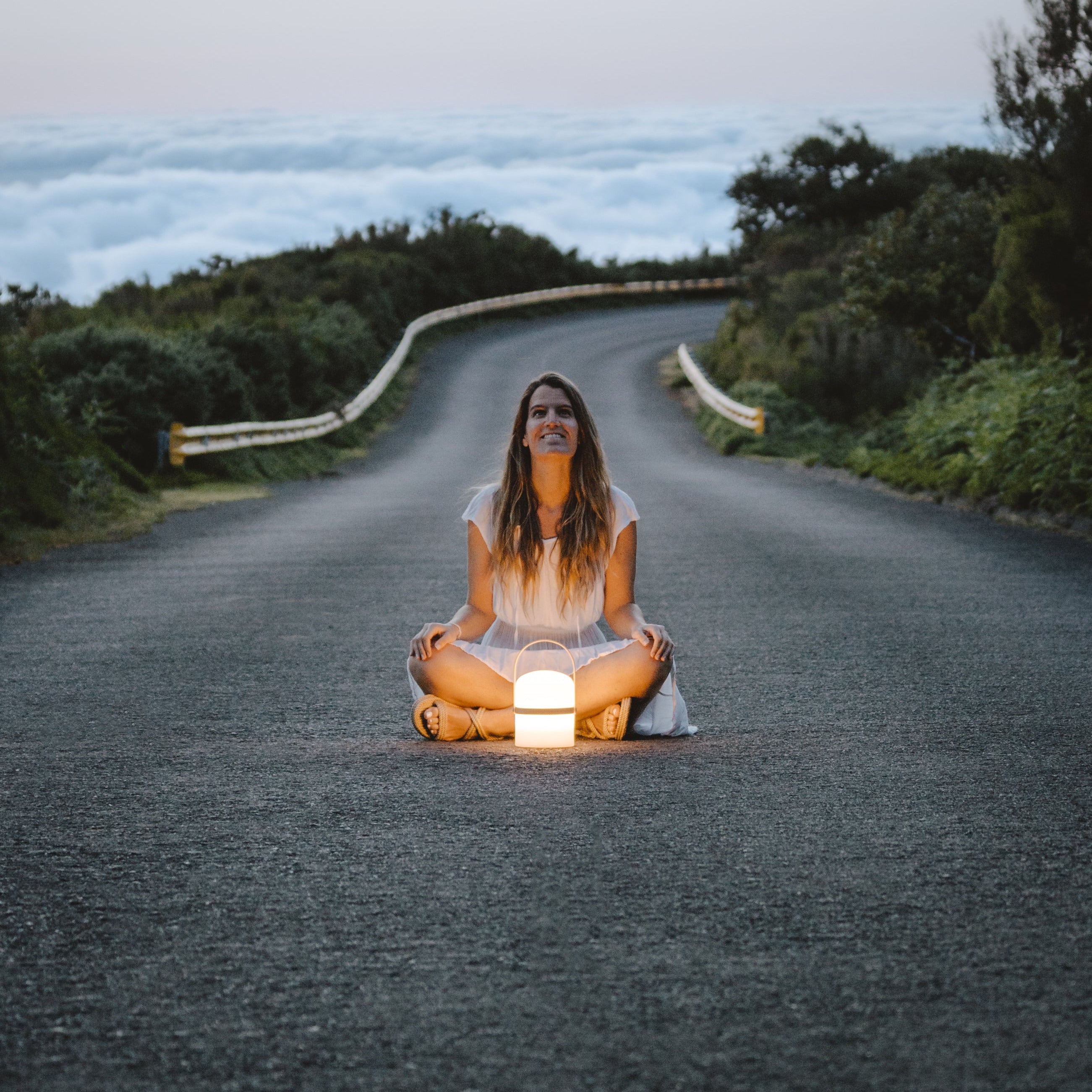 Frau sitzt meditierend mit tragbarer LED-Leuchte Luma auf einer Straße in der Natur – warmes Licht für bewusste Outdoor-Momente