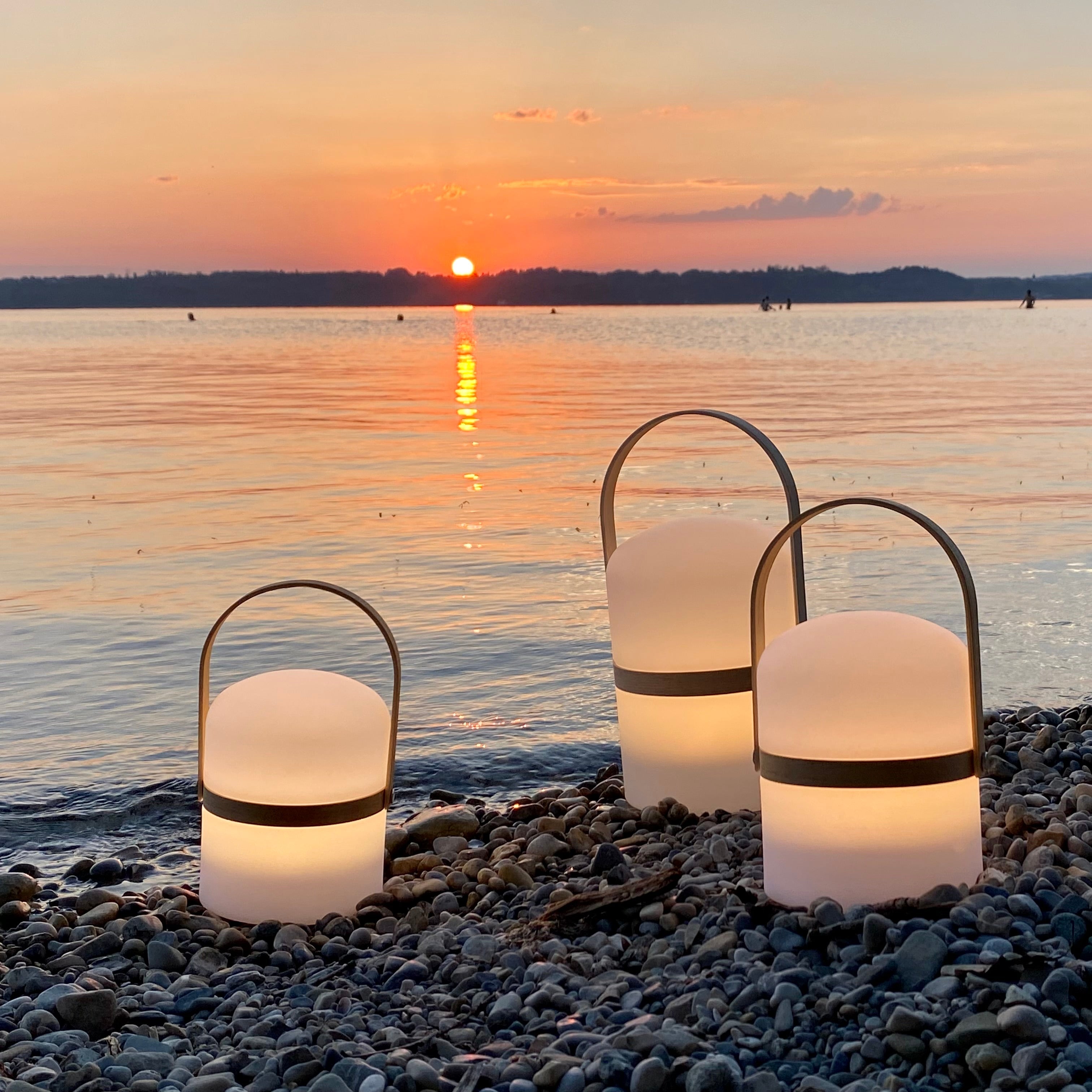 Drei tragbare LED-Leuchten Luma am Seeufer bei Sonnenuntergang – stilvolle Outdoor-Beleuchtung mit warmweißem Licht