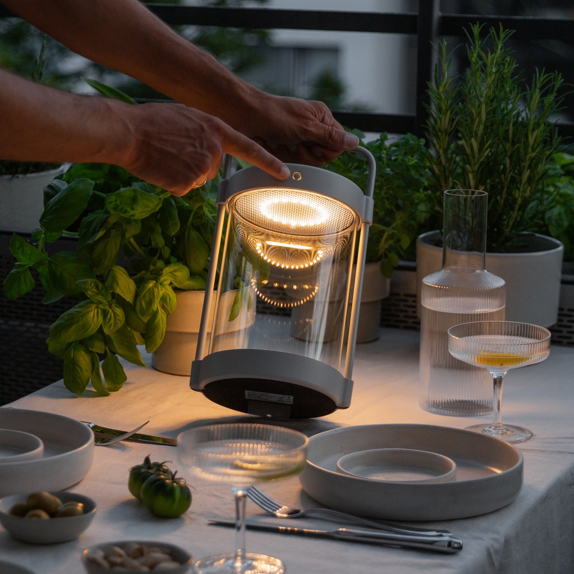 Caia LED-Solarlaterne in Grau mit Echtglas – stimmungsvolle Beleuchtung auf gedecktem Terrassentisch bei Abenddämmerung.