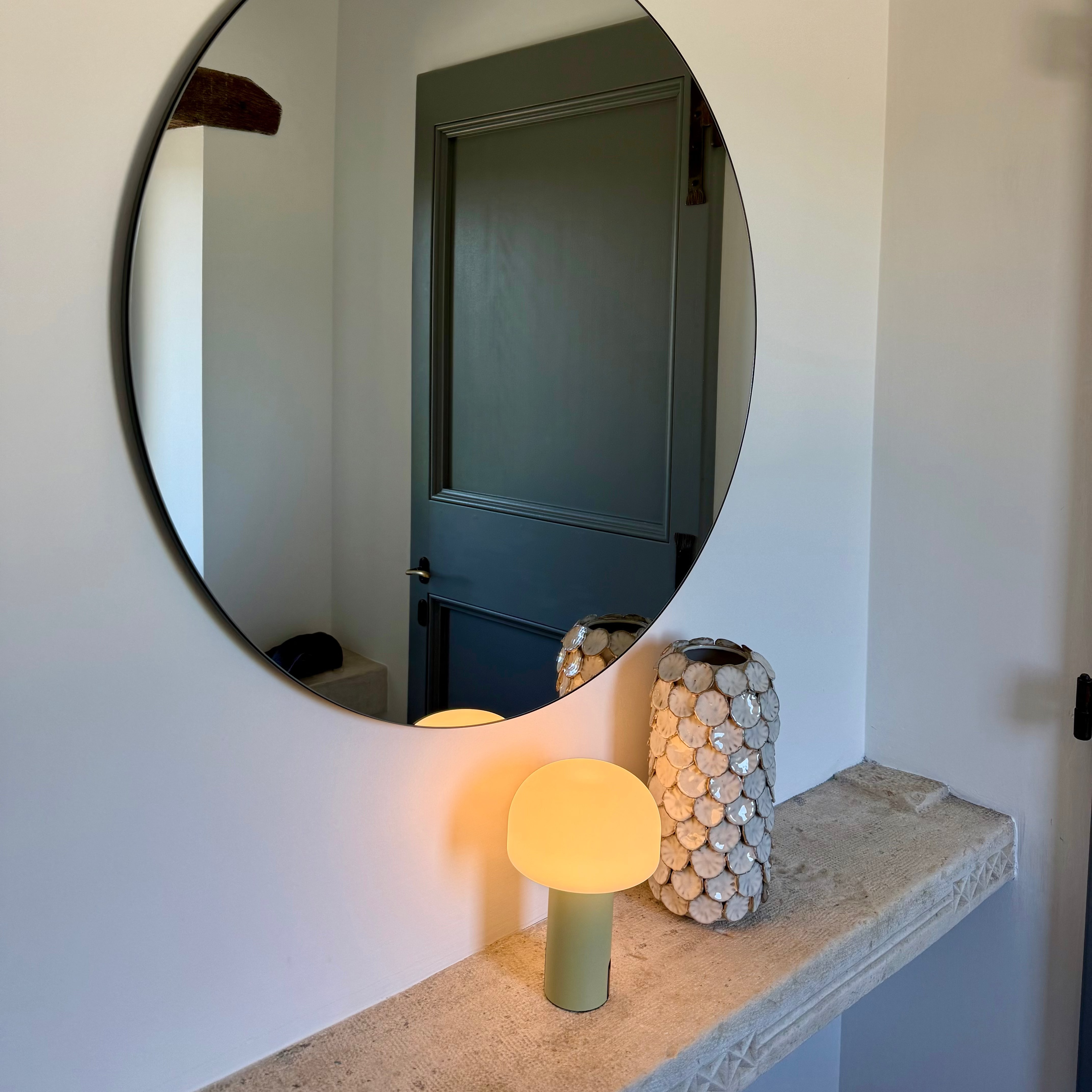 Die Noa Lampe auf eine, Sideboard aus Stein in einem stilvollen Ambiente im Eingangsbereich eines Hauses mit rundem Spiegel und einer Designer Vase.
