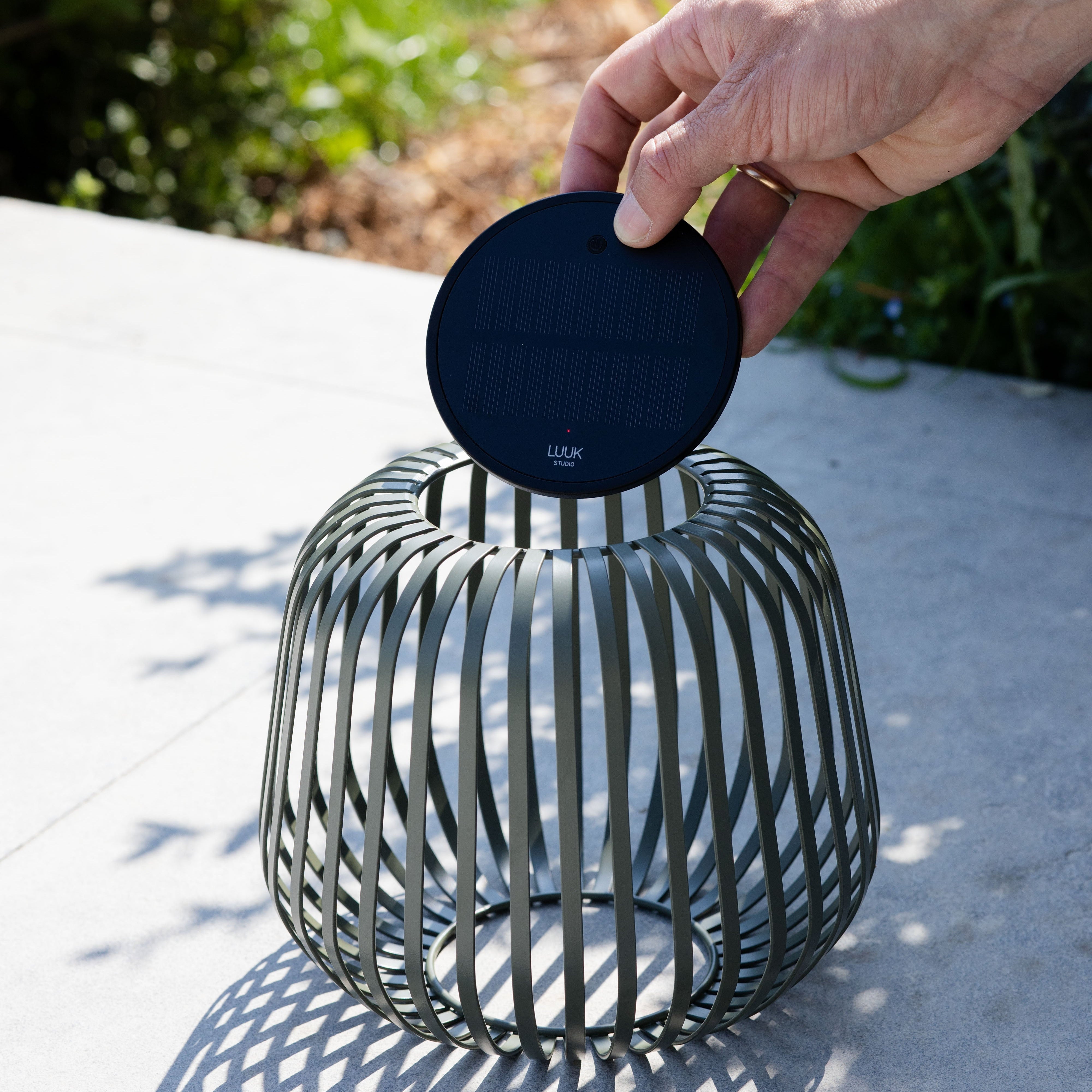 Solis Solarlaterne von LUUK Studio in grün s auf einer Terrasse – entnehmbares Solarmodul wird gezeigt, ideal für stimmungsvolle Beleuchtung im Garten oder Outdoor-Bereich.