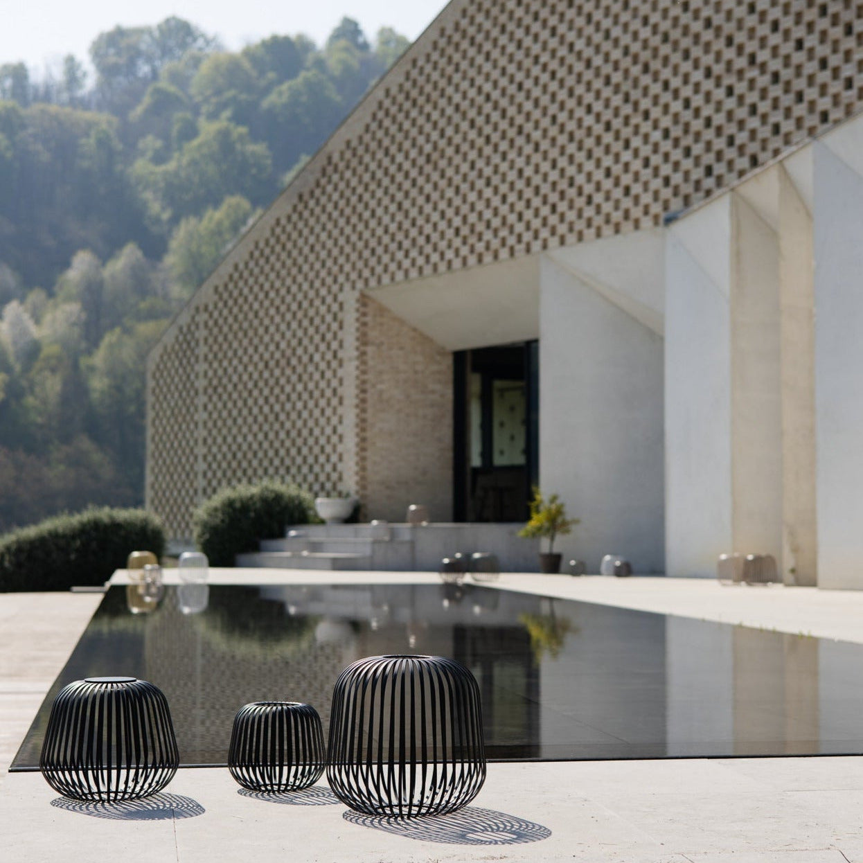 Drei schwarze Solis Solarlaternen vor moderner Architektur und Pool – stilvolle Outdoor-Designbeleuchtung für Garten, Terrasse oder Hotelanlage