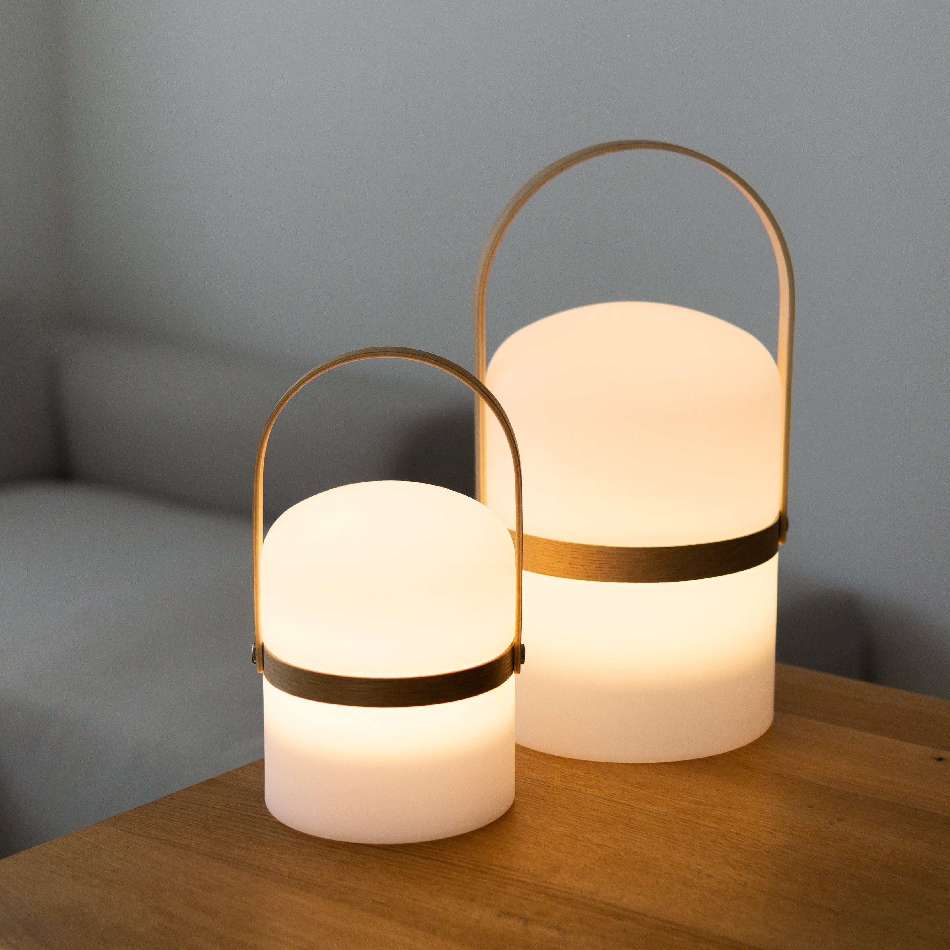 Zwei angeschaltete Luma LED Laternen mit warmweißen Licht in der Größe M und L auf Holztisch als Stimmungslicht im Wohnzimmer Ambiente