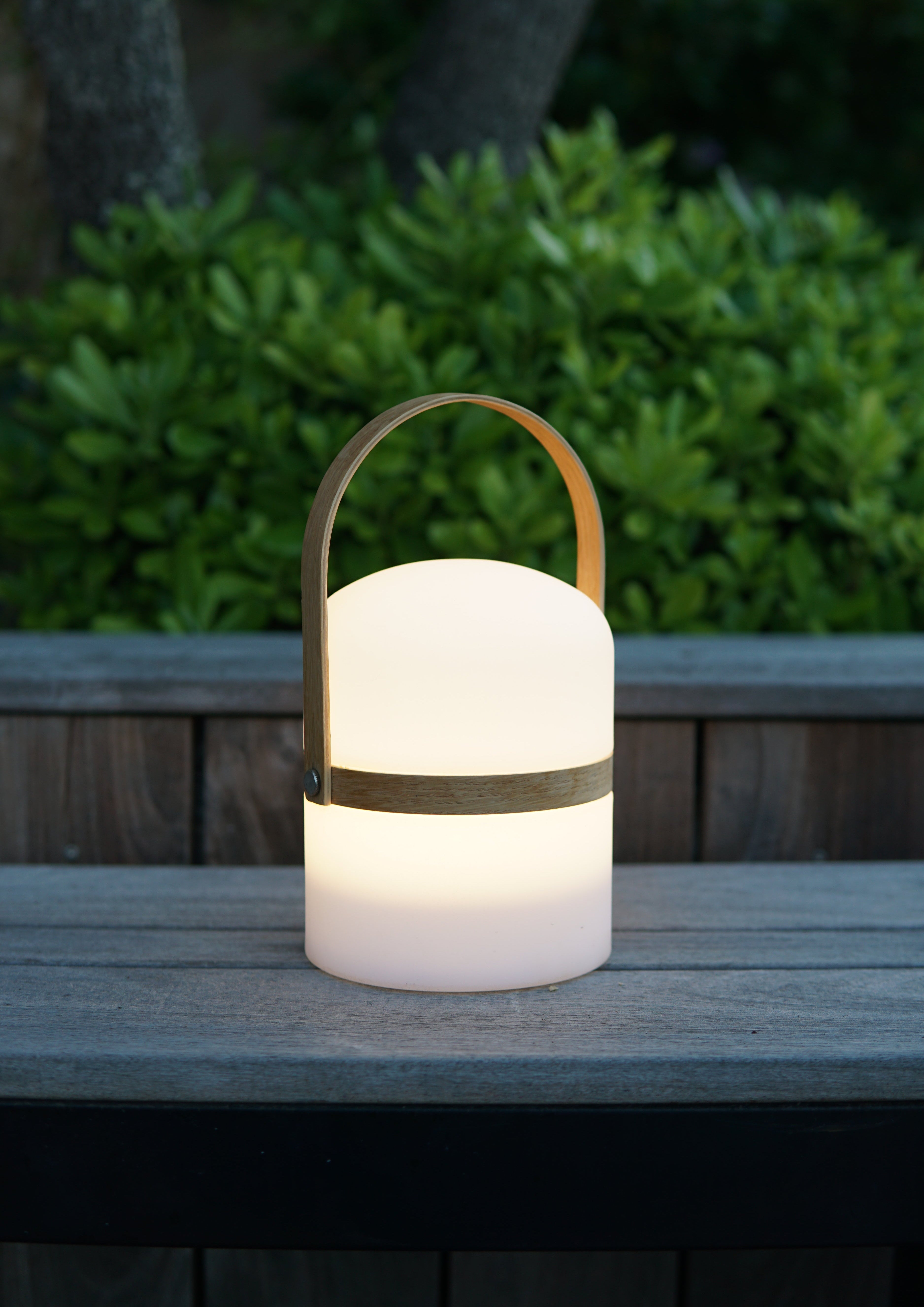 Nahaufnahme im Garten der leuchtenden Luma LED Design-Laterne mit warmweißen Licht, hergestellt aus recyceltem Meeresplastik und mit nachhaltigem Holzgriff.