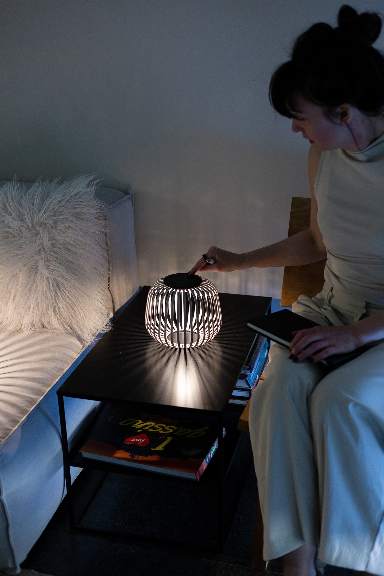 Hand einer Frau dimmt das eingesetzte Solarmodul der Solis LED Tischlaterne in weiß mit Schattenwurf im Wohnzimmer auf Sideboard