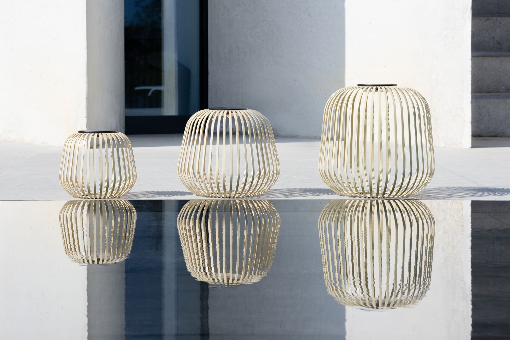 Drei Solis Solarlaternen in Beige-Sand vor moderner Architektur mit stilvoller Wasserreflexion im Naturpool