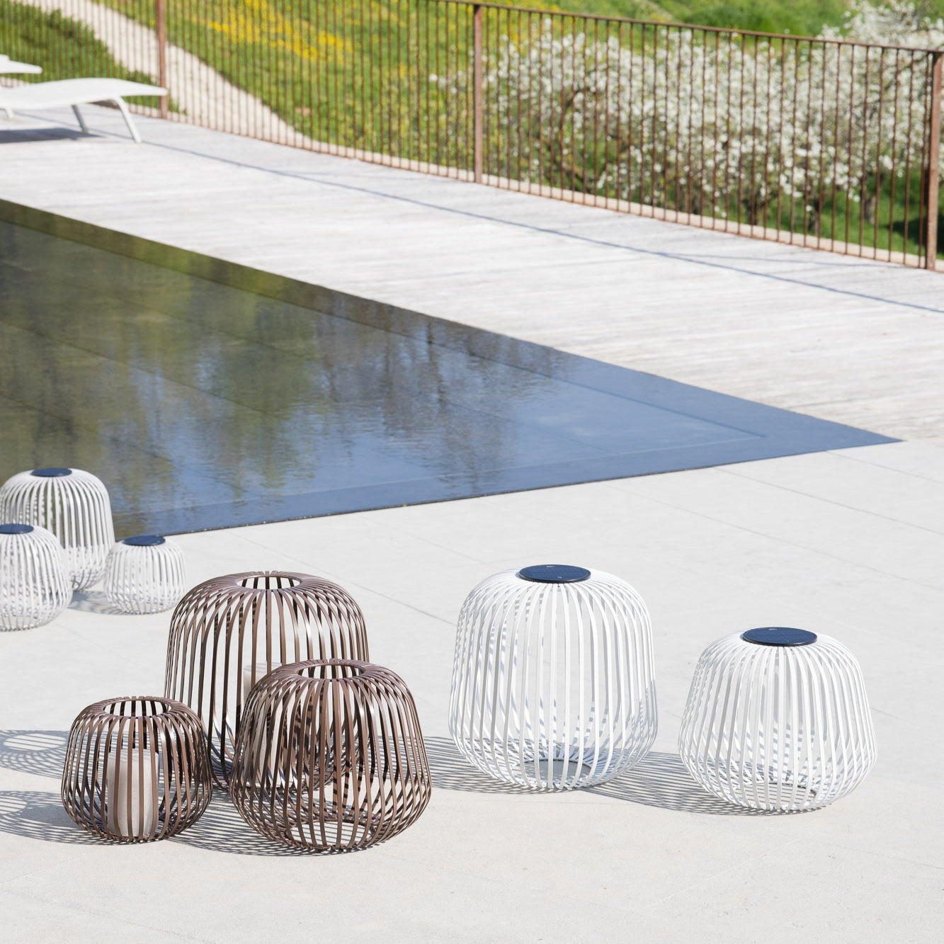 Solis Solarlaternen in Braun und Weiß in verschiedenen Größen neben einem modernen Pool im Sonnenlicht