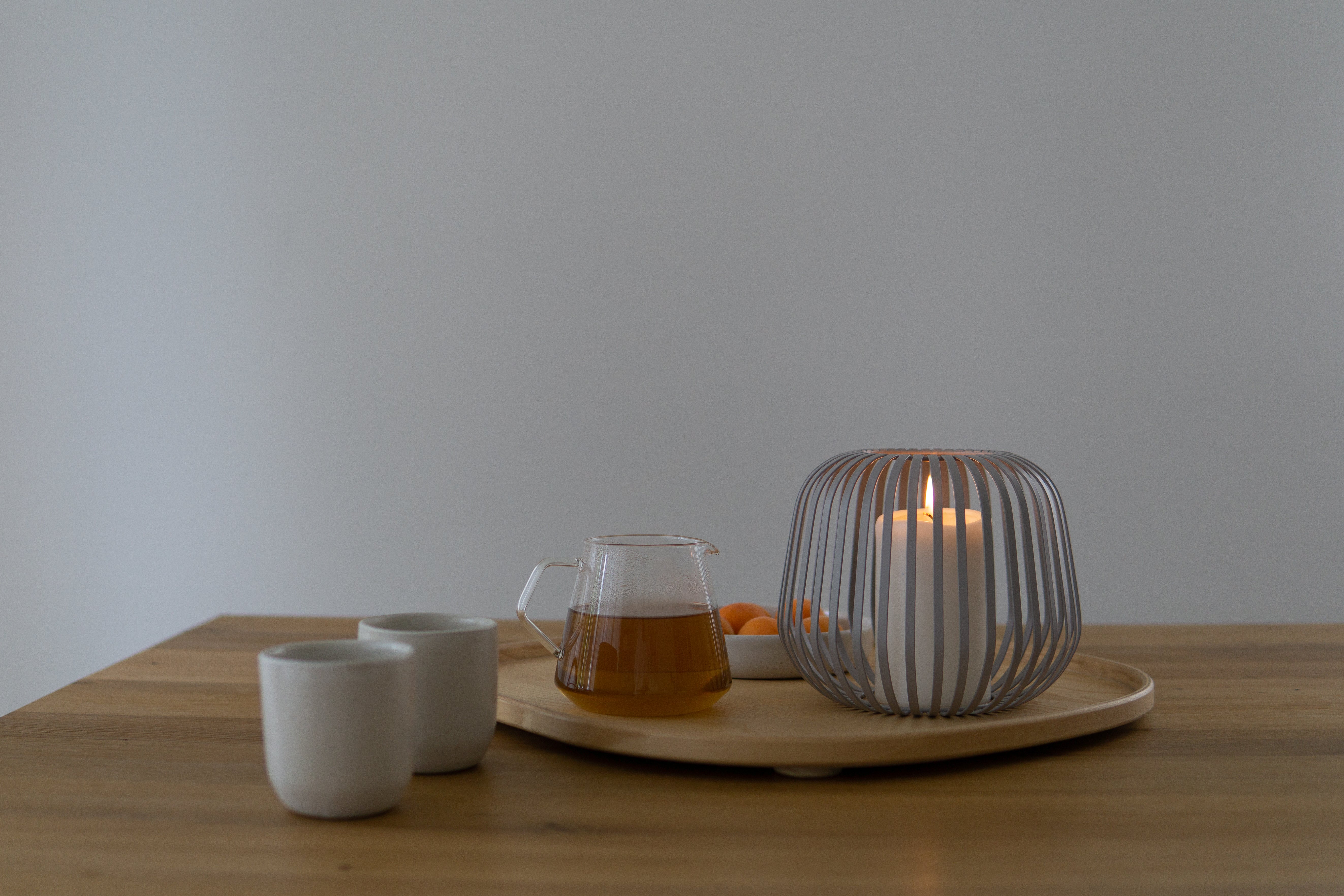die Luuk Studio Solis Laterne in grau steht mit brennender Kerze auf Esstisch aus Holz mit Teekanne und Teebechern.