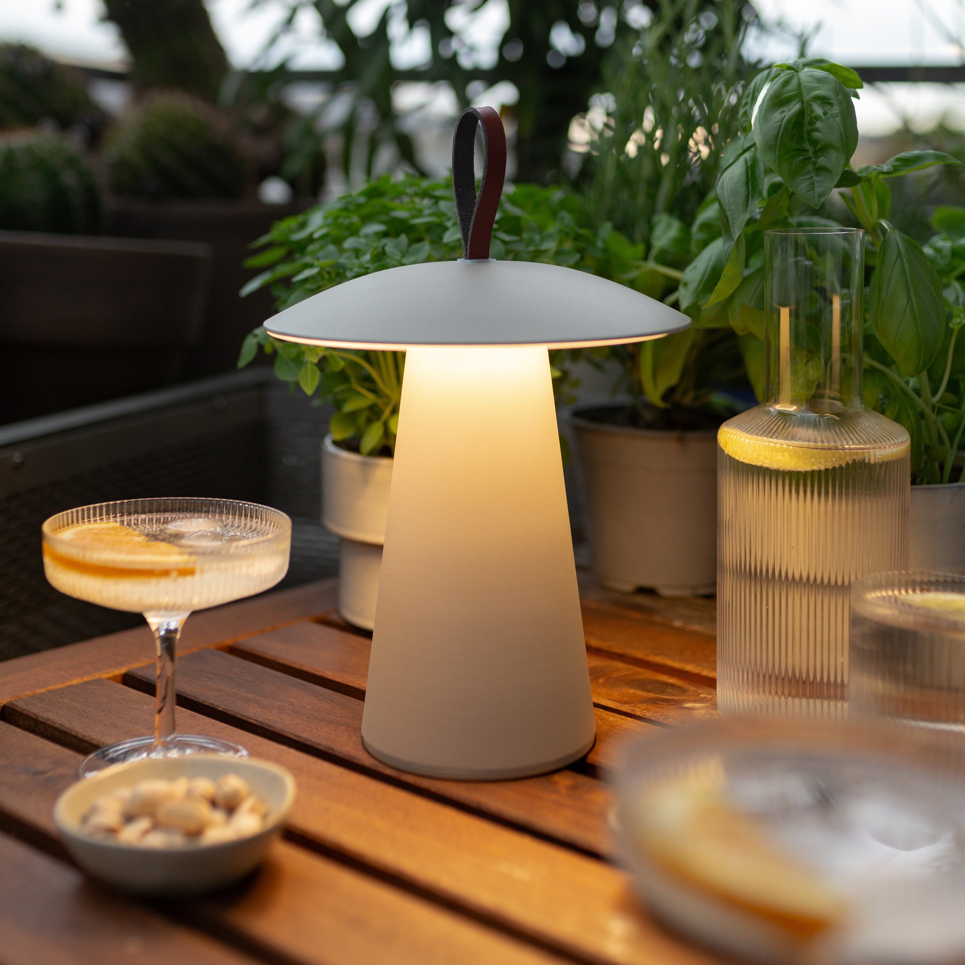 Dimmbare LED-Tischlampe Lyvo in Weiß – stimmungsvolle Outdoor-Leuchte auf Holztisch mit Drinks und Kräutern