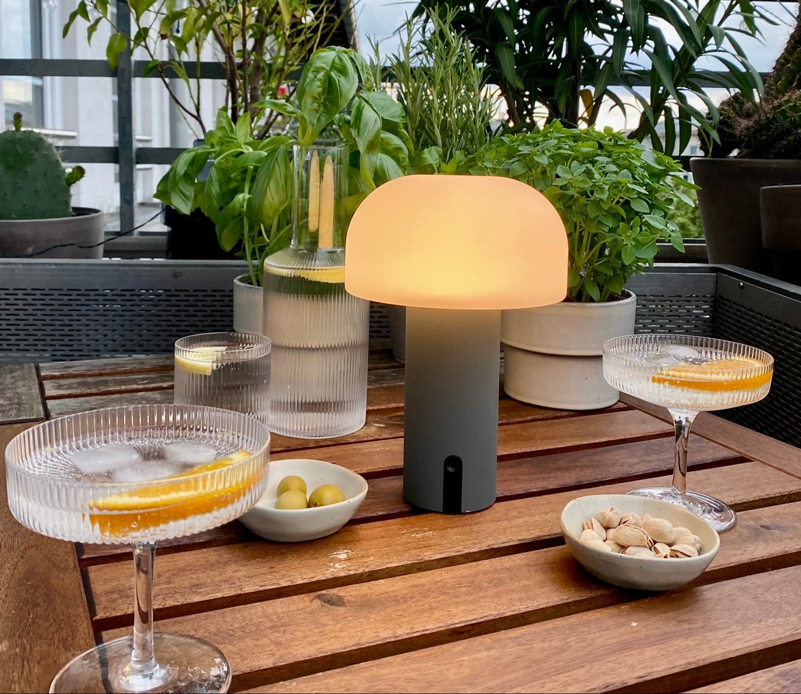 Stufenlos dimmbare Noa Tischleuchte in grau ohne Kabel auf Balkontisch mit Snacks und Drinks in Abenddämmerung