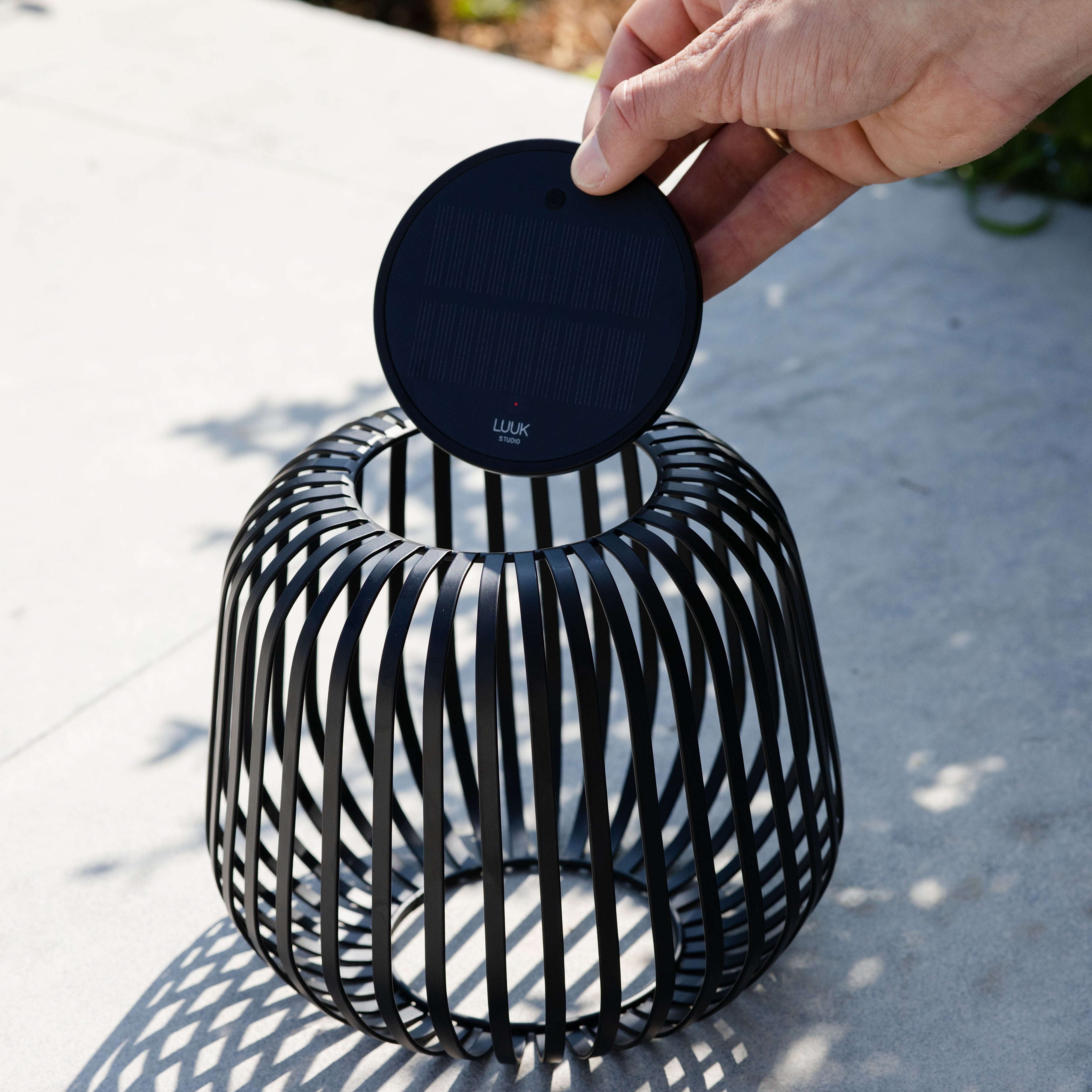 Solis Solarlaterne von LUUK Studio in Schwarz s auf einer Terrasse – entnehmbares Solarmodul wird gezeigt, ideal für stimmungsvolle Beleuchtung im Garten oder Outdoor-Bereich.