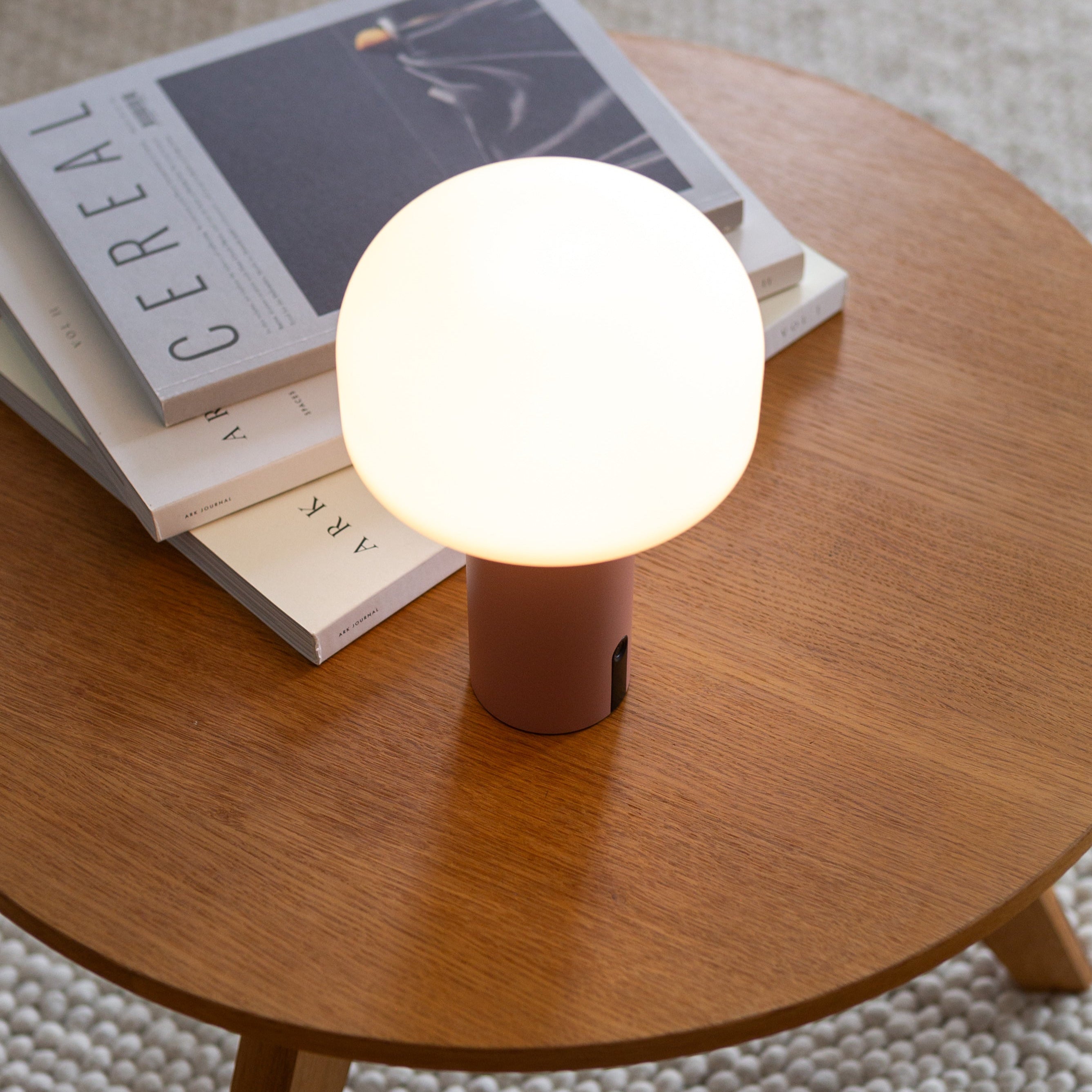 Dimmbare Noa LED-Tischlampe in Koralle auf Couchtisch mit Coffeebooks– stilvolle Akkuleuchte für stimmungsvolles Licht im Wohnzimmer