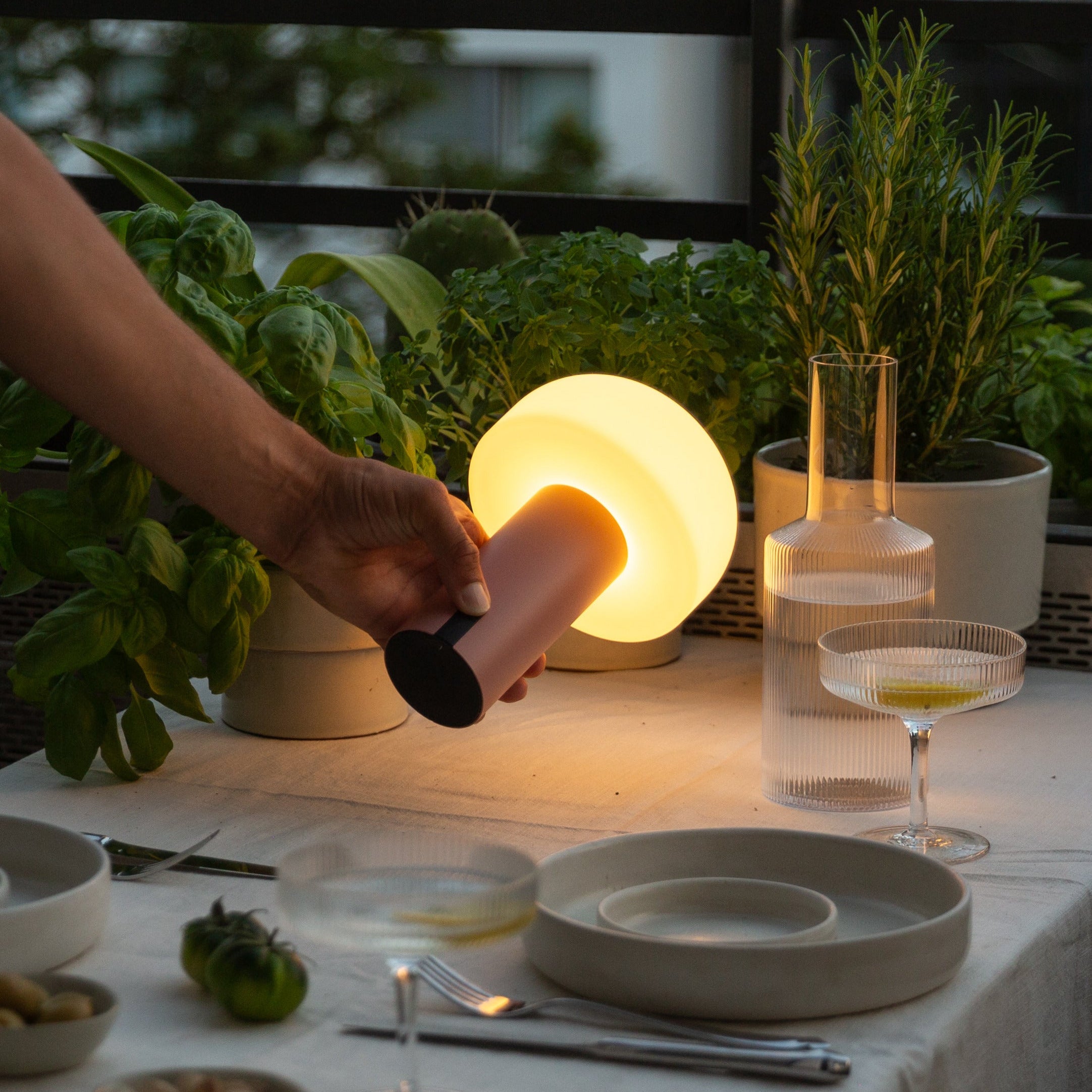 Noa LED-Tischlampe in Terracotta beim Einsatz als stimmungsvolle Beleuchtung auf einem gedeckten Tisch – tragbar, dimmbar und ideal für Abendessen im Innen- oder Außenbereich