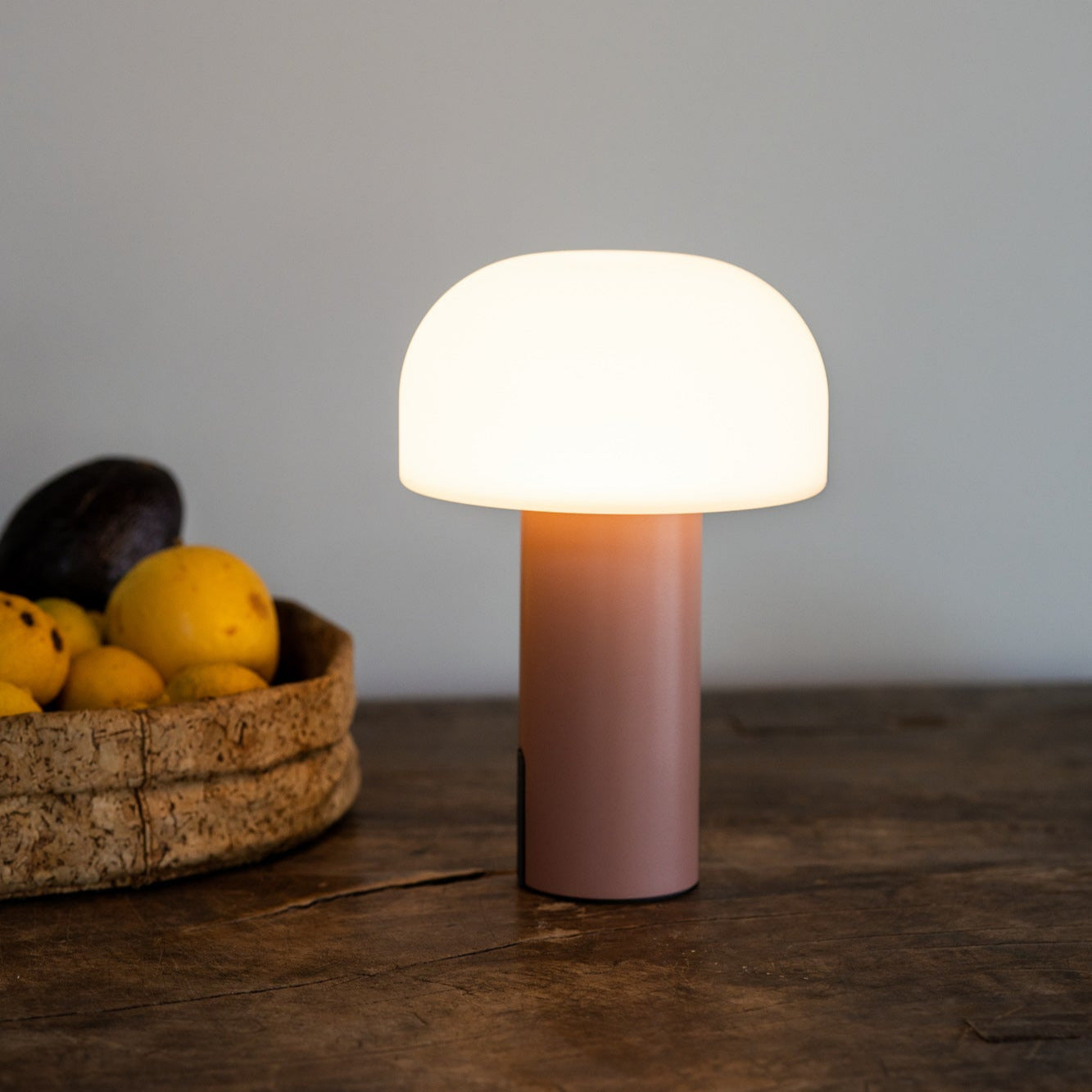 Minimalistische Noa LED-Tischleuchte von Luuk Studio mit pilzförmigem Schirm in Koralle mit warmweißem Licht auf rustikalem Holztisch, ideal als sanfte Lichtquelle für Wohnzimmer, Eingangsbereich, Flur oder Kommode.