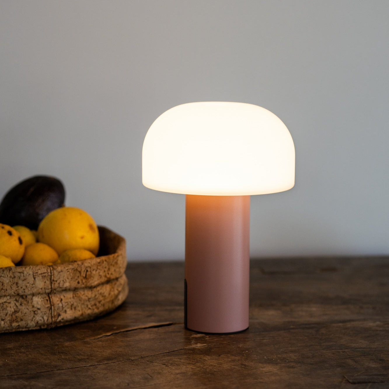 NOA Tischleuchte von LUUK Studio mit mattem Glasschirm auf rustikalem Holztisch neben Obstschale