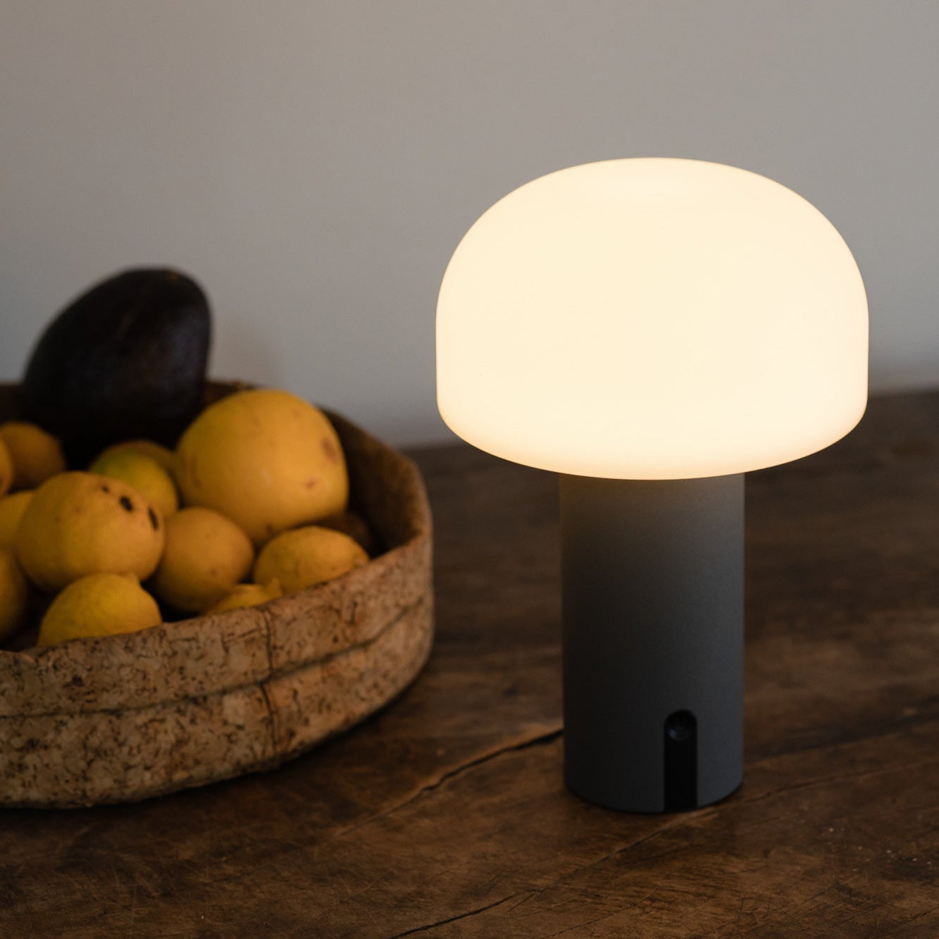NOA Tischleuchte von LUUK Studio mit mattem Glasschirm auf rustikalem Holztisch neben Obstschale
