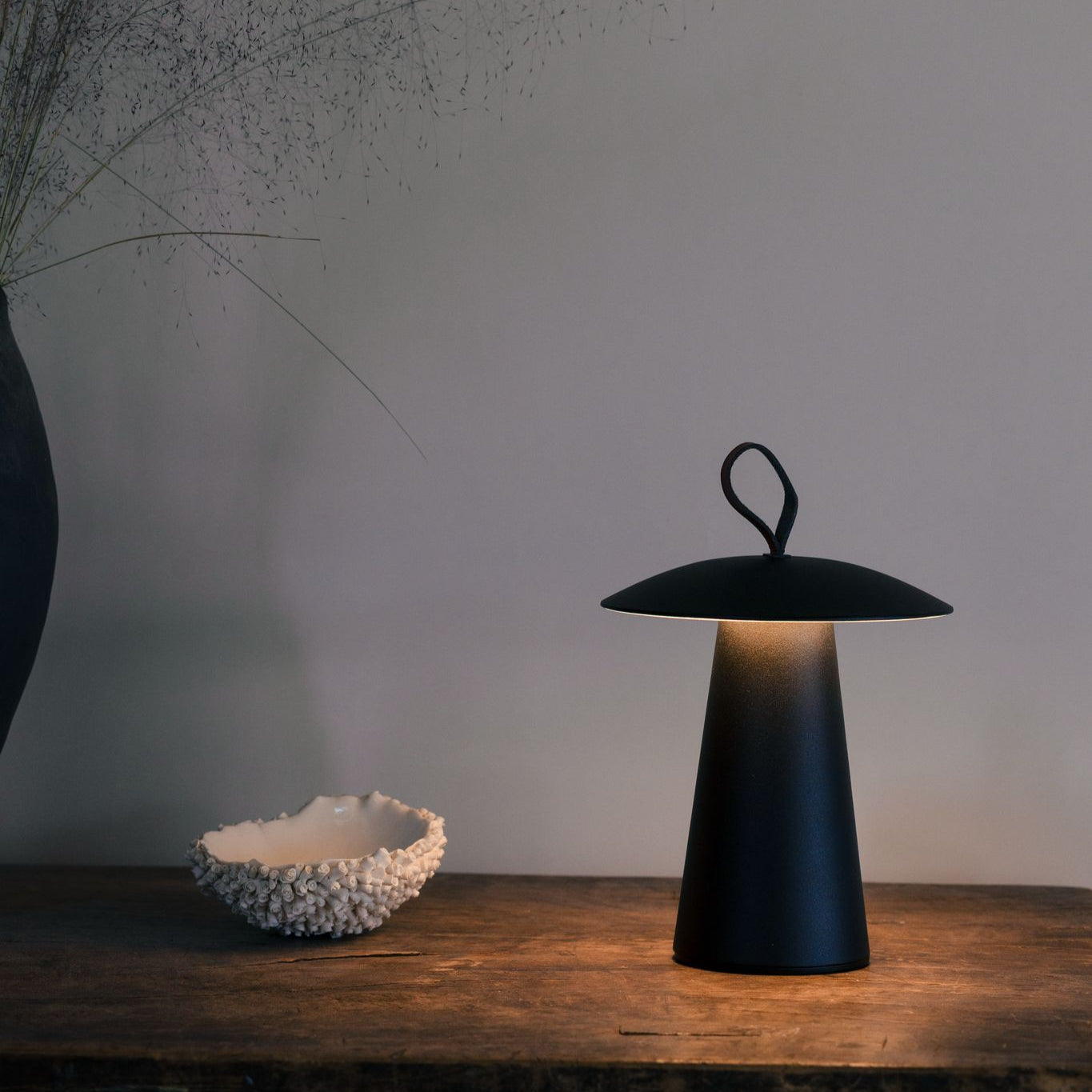 Schwarze mobile LED-Solarlampe von LUUK Studio auf Holztisch, warmweiß leuchtend