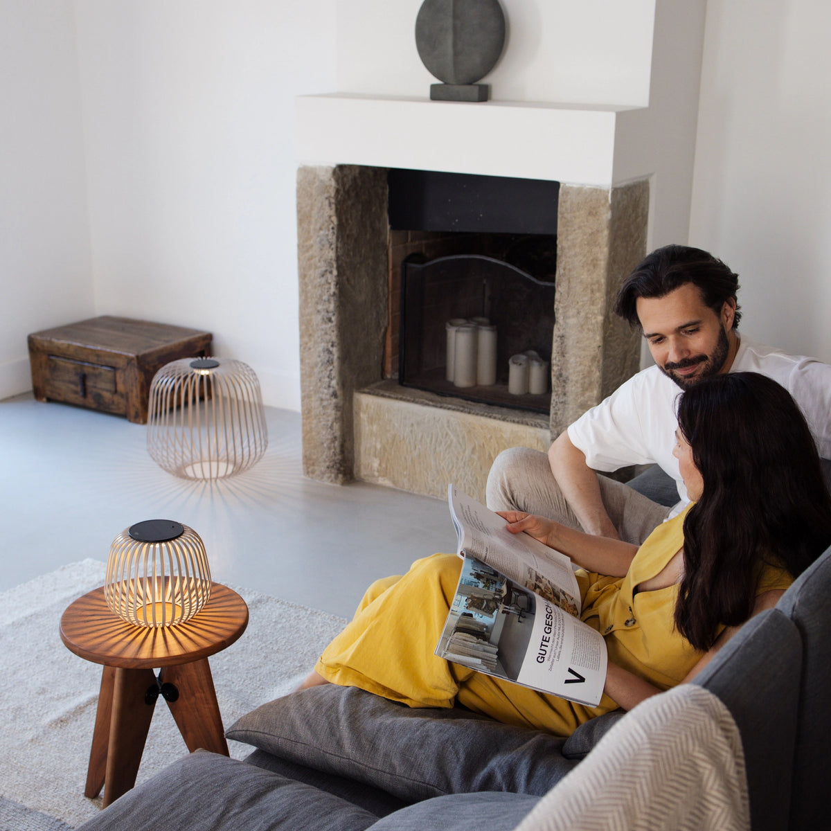 Lifestylebild: Pärchen lesend auf Sofa im Wohnzimmer, daneben SOLIS Solarleuchte in S und XL in der Farbe Nomad mit Schattenwurf durch das Licht des Solarmoduls