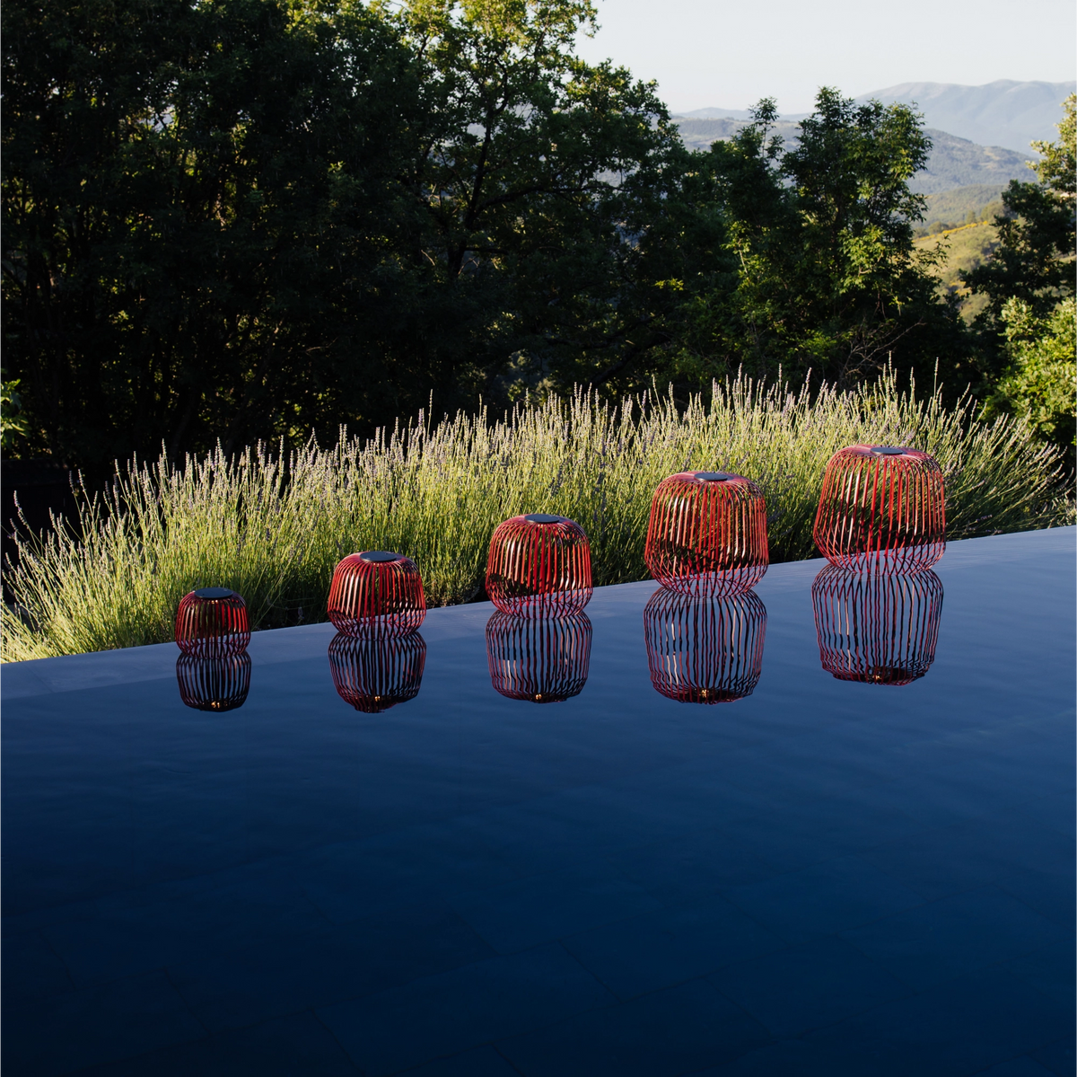 5er Set SOLIS Solarleuchte von LUUK Studio in den Größen S, M, L, XL, XXL in Schwarzkirsche an Pool mit Spiegelung im Wasser