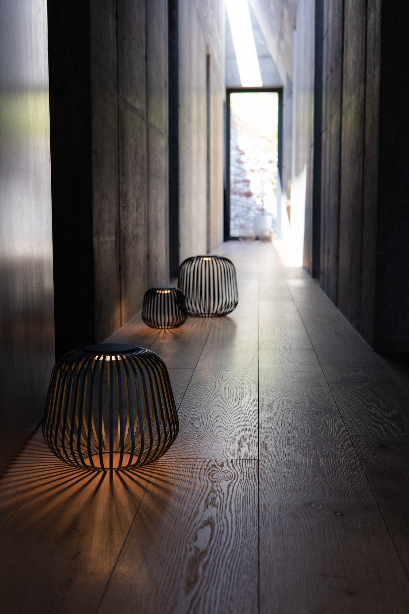 Drei Solarlaternen Solis in verschiedenen Größen beleuchten einen modernen, dunklen Flur mit warmem Licht und dekorativem Schattenwurf – ideal für stilvolle Akzentbeleuchtung im Innenbereich.