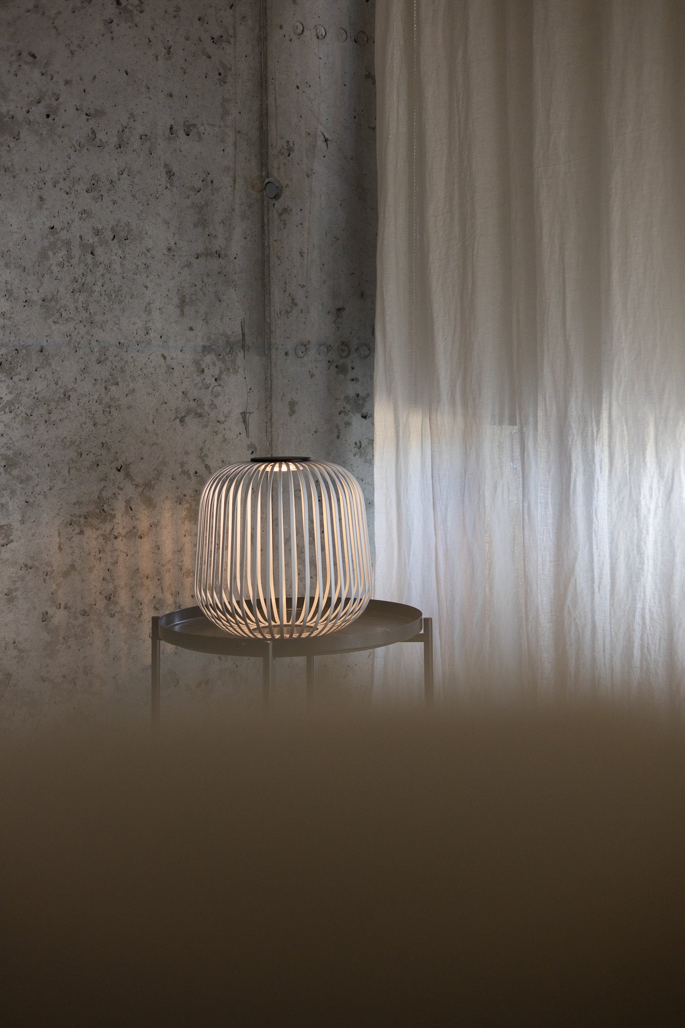 Solarlaterne Solis im Industrial-Stil auf einem runden Beistelltisch vor Betonwand und Vorhang – erzeugt stimmungsvolles, warmweißes Licht für moderne Wohn- oder Loungebereiche.