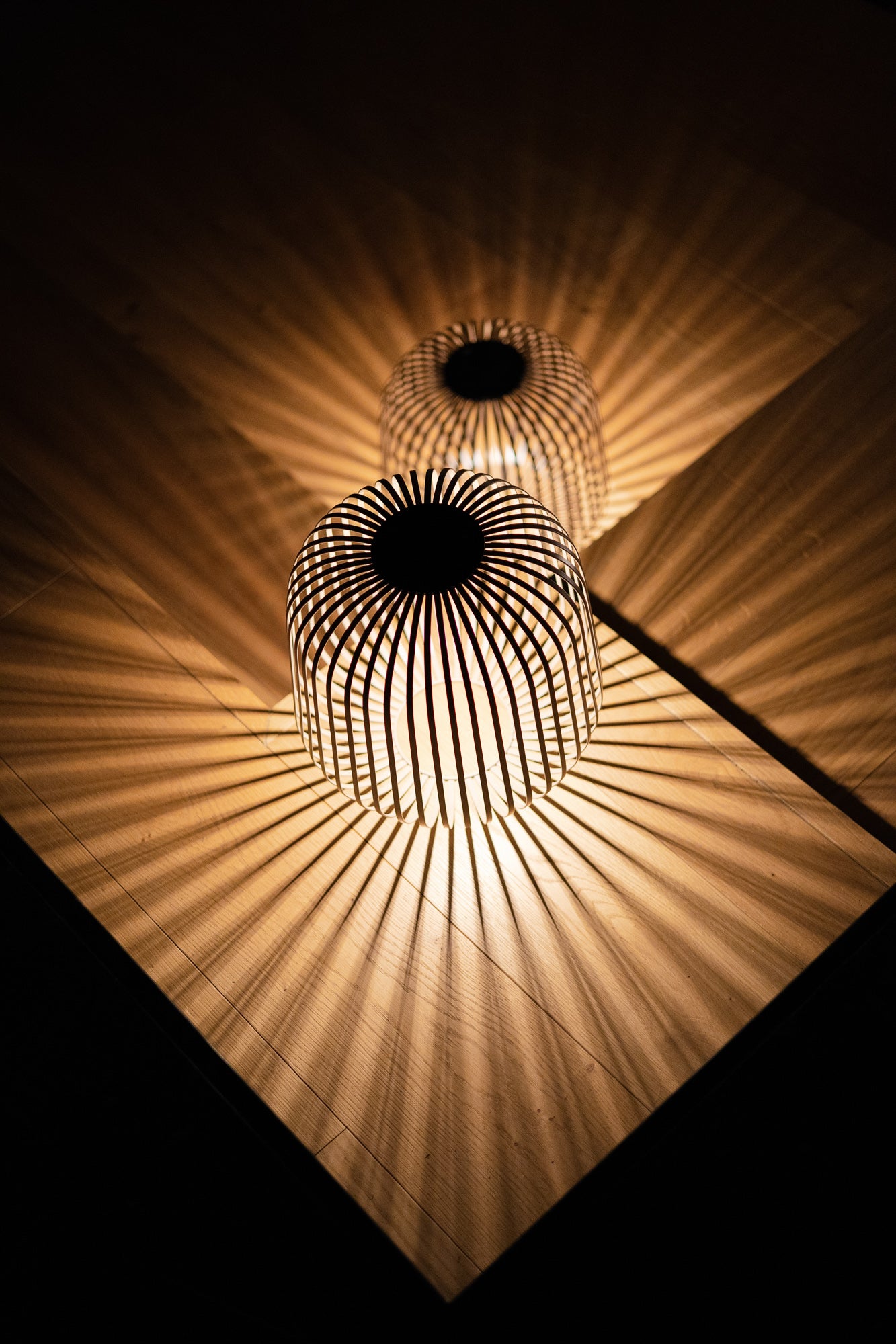 Zwei beleuchtete Solarlaternen Solis werfen bei Dunkelheit eindrucksvolle, symmetrische Schattenmuster auf einen Holzfußboden – ideal für stimmungsvolle Abendbeleuchtung im Innen- oder Außenbereich.