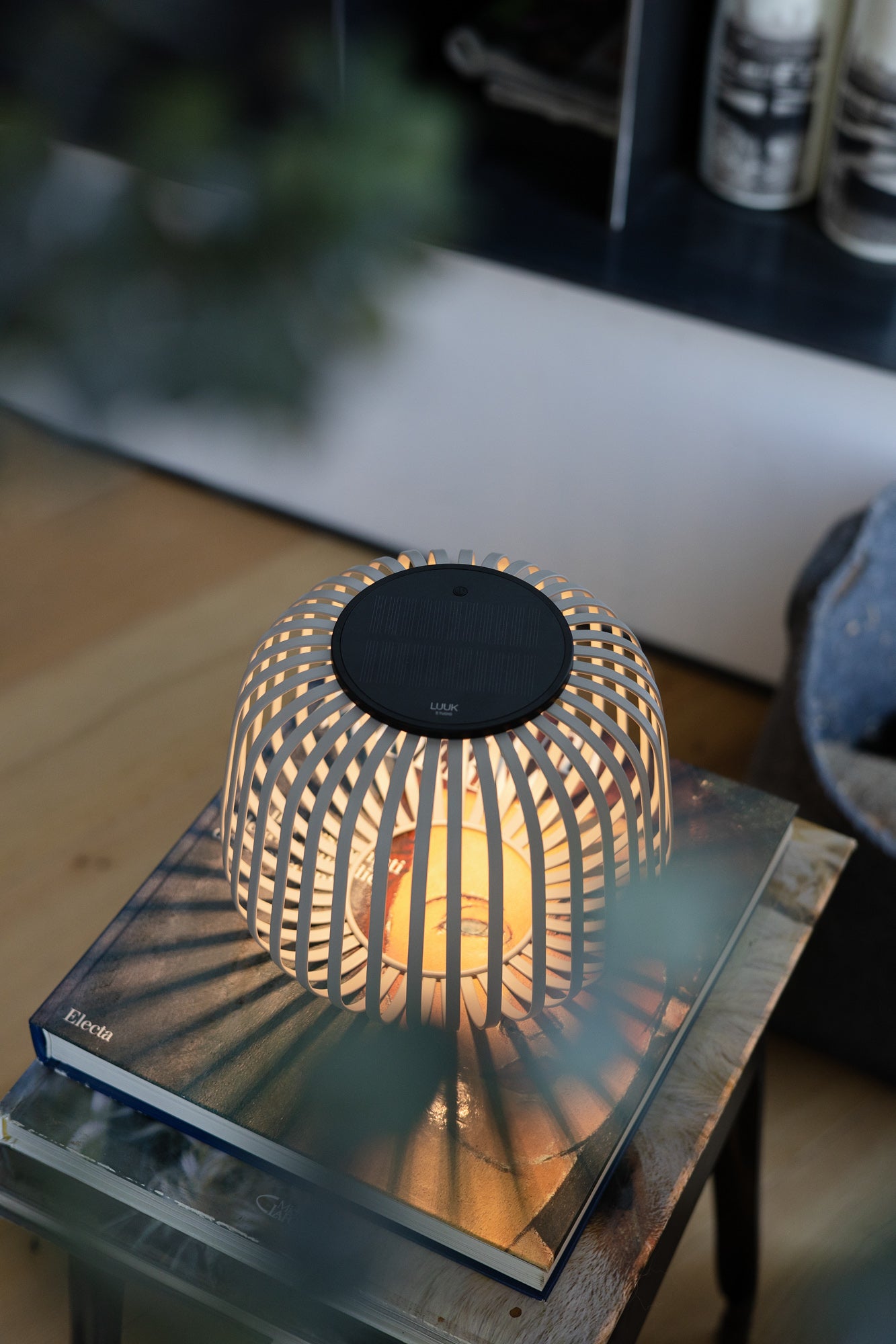 Die Solarlaterne Solis spendet warmes, dimmbares Licht auf einem Couchtisch mit Bildband im Wohnzimmer – ideal als dekoratives Stimmungslicht oder Windlicht mit Schatteneffekt.