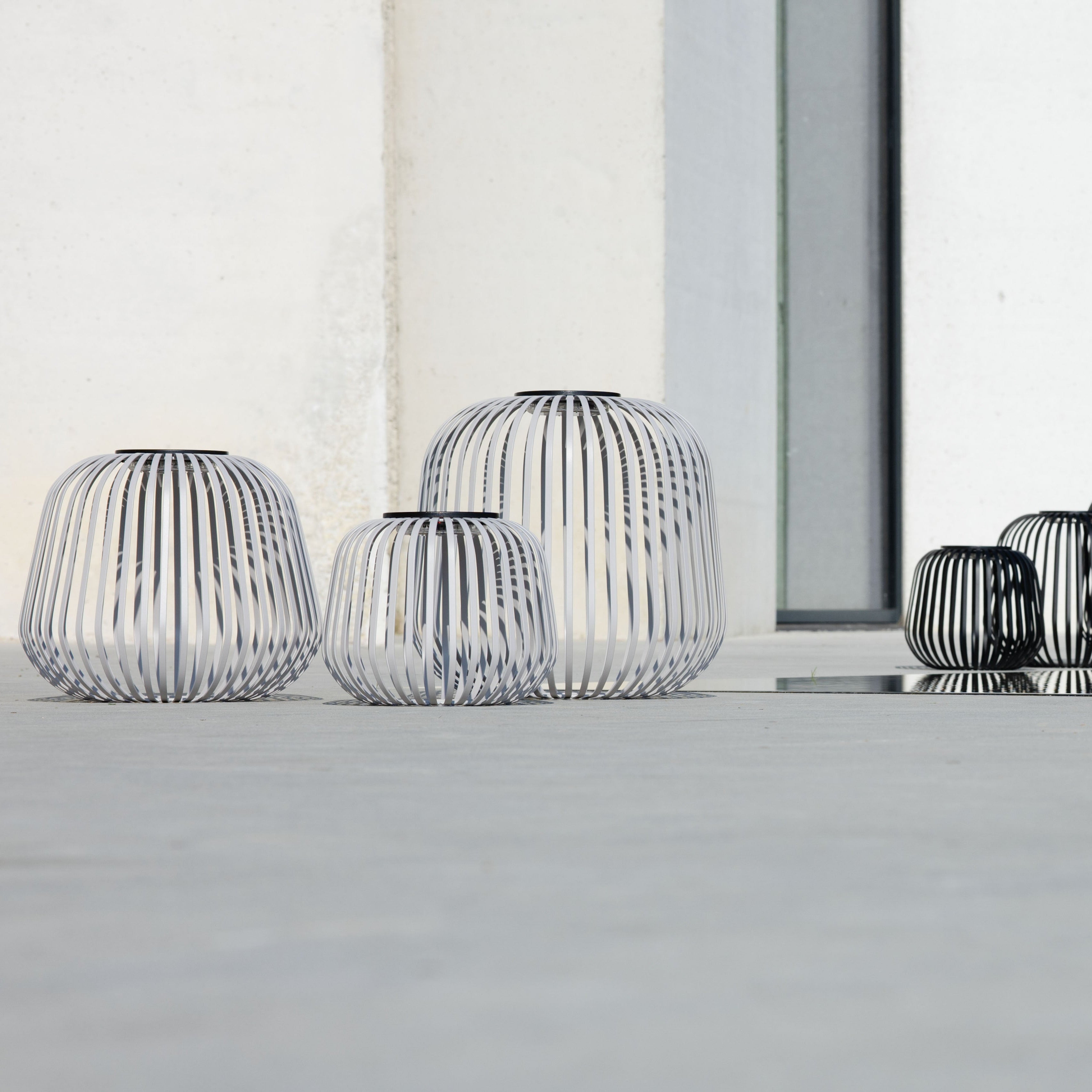 Mehrere Solis Solarlaternen von LUUK Studio in Weiß und Schwarz in verschiedenen Größen auf moderner Terrasse – stilvolle Gartenbeleuchtung mit dekorativem Design für den Außenbereich.