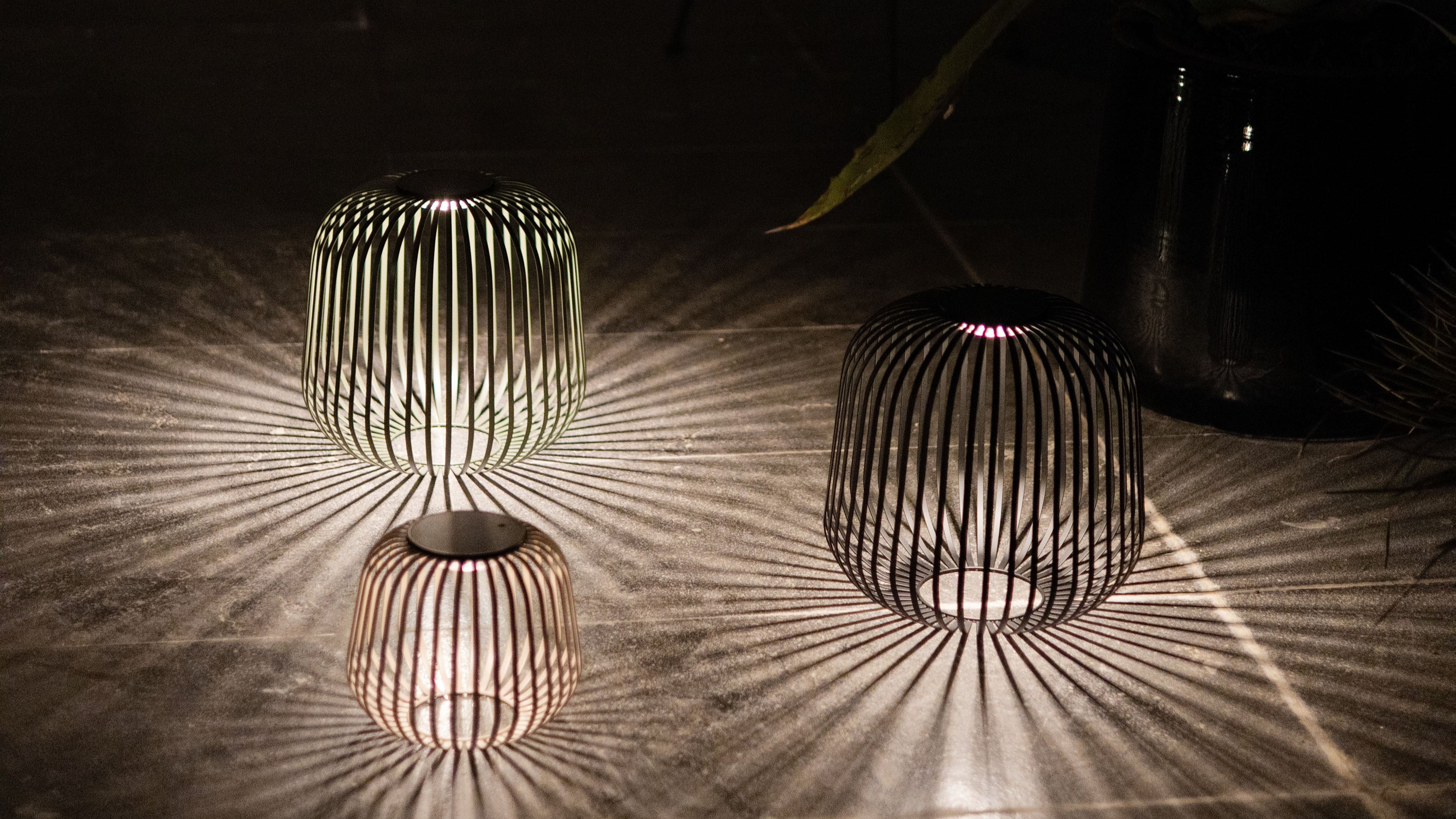 Drei Solarlaternen in Haselnuss, Schwarz und Grün erzeugen atmosphärisches Lichtspiel mit markanten Schatteneffekten – perfekte Akzentbeleuchtung für Garten, Terrasse oder Outdoor-Dinner