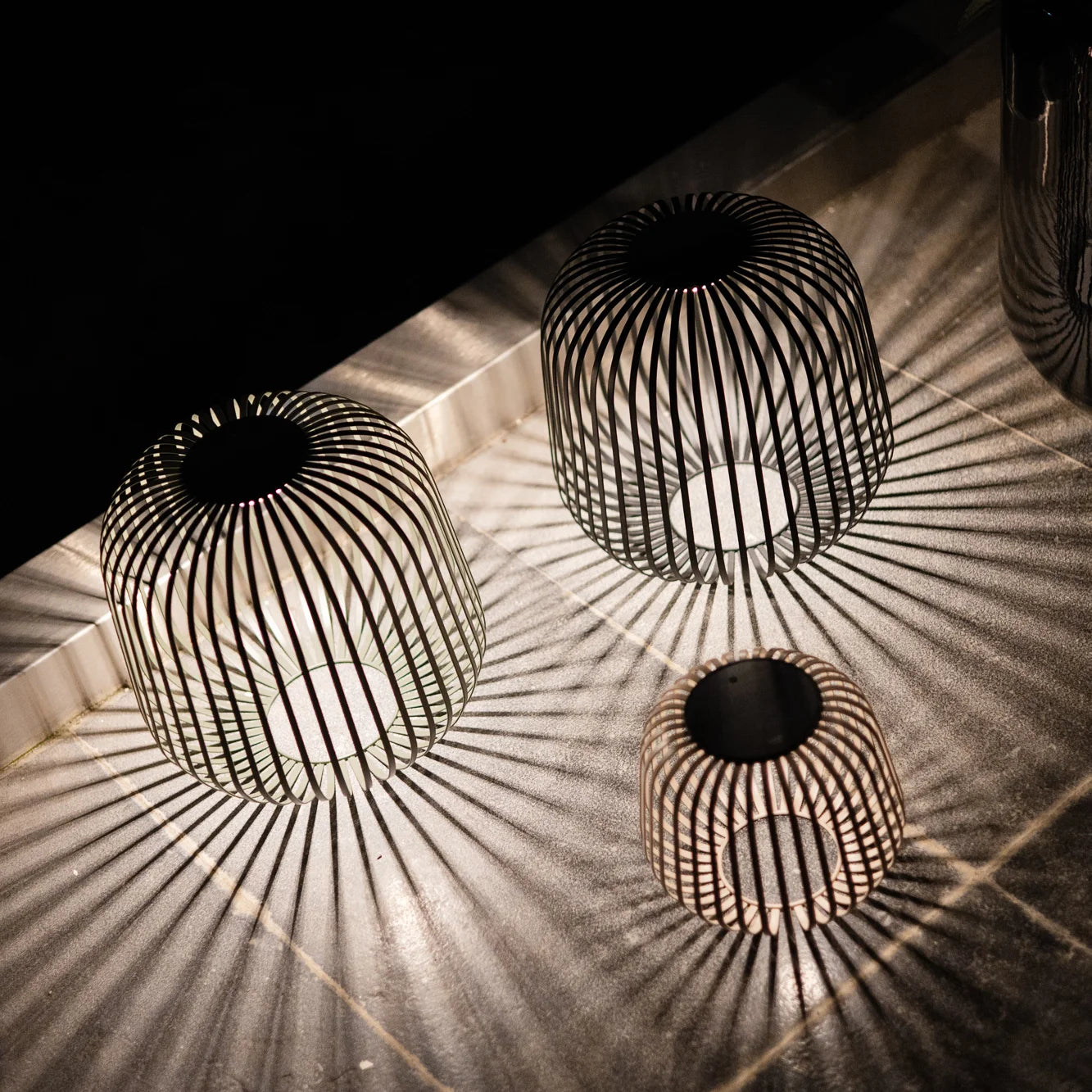 Drei Solarlaternen in Haselnuss, Schwarz und Grün erzeugen atmosphärisches Lichtspiel mit markanten Schatteneffekten – perfekte Akzentbeleuchtung für Garten, Terrasse oder Outdoor-Dinner