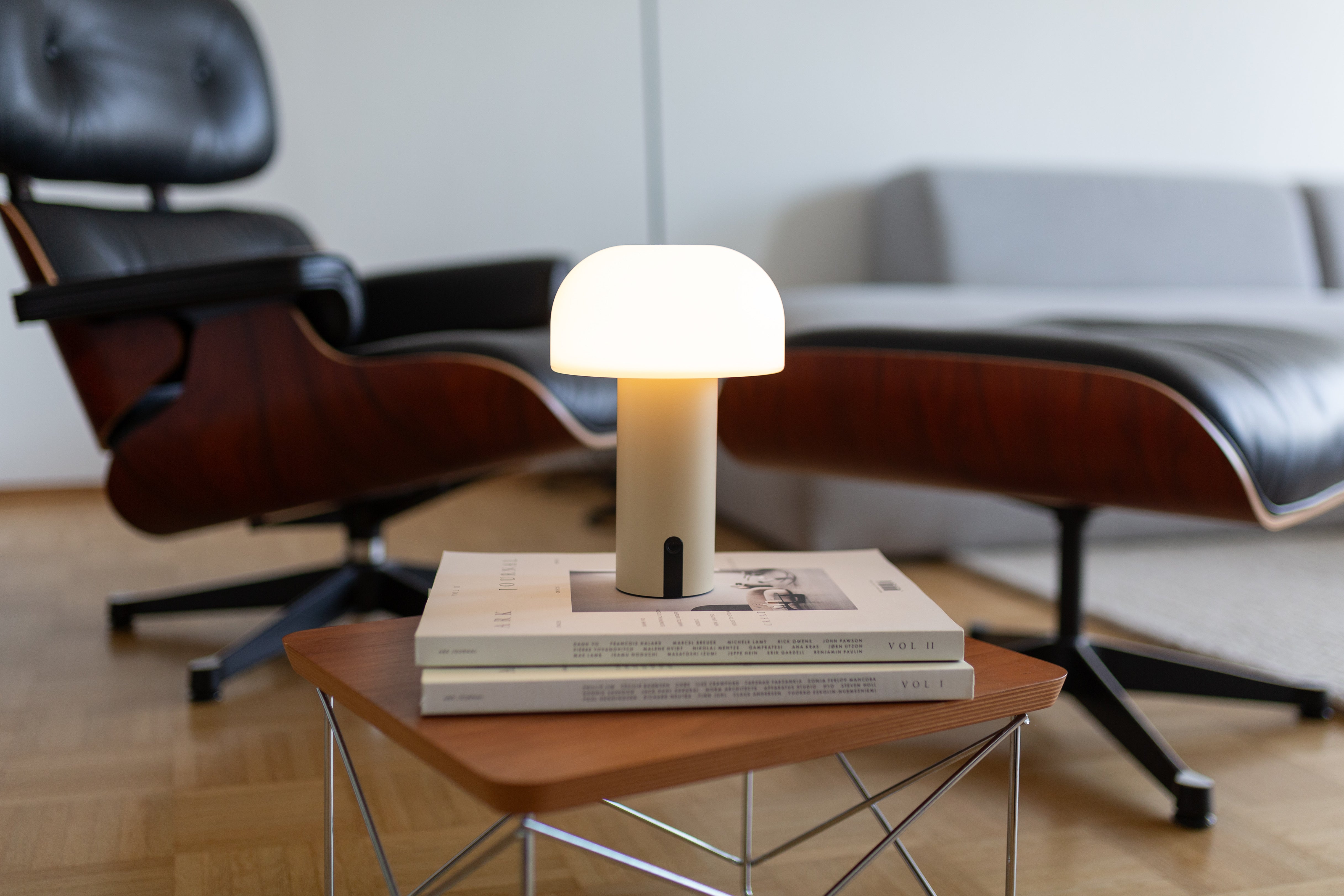 Moderne LED-Tischlampe von LUUK Studio in Beige – dimmbare Designleuchte auf Couchtisch vor Ledersessel mit Hocker im Wohnzimmer