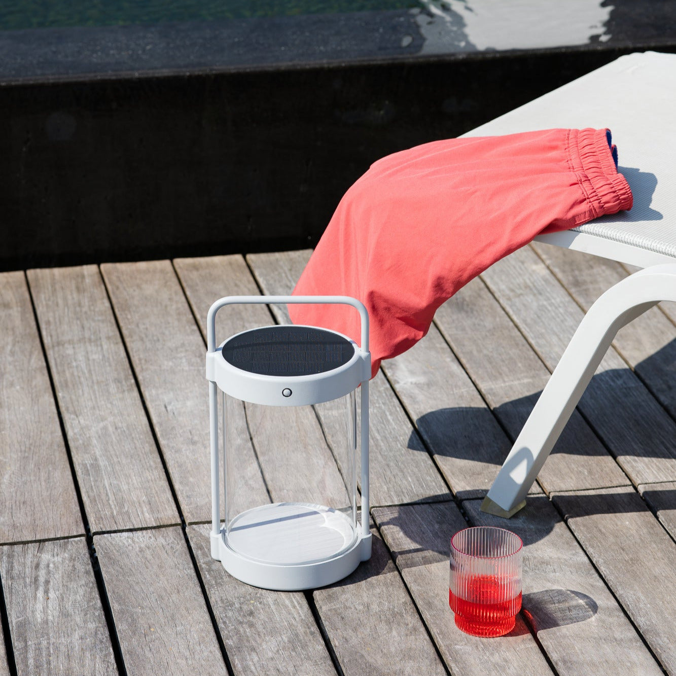 Caia LED-Solarlaterne in Grau mit Echtglas auf Holzdeck neben Sonnenliege und Getränk – perfekte stimmungsvolle Beleuchtung für den Außenbereich im Sommer