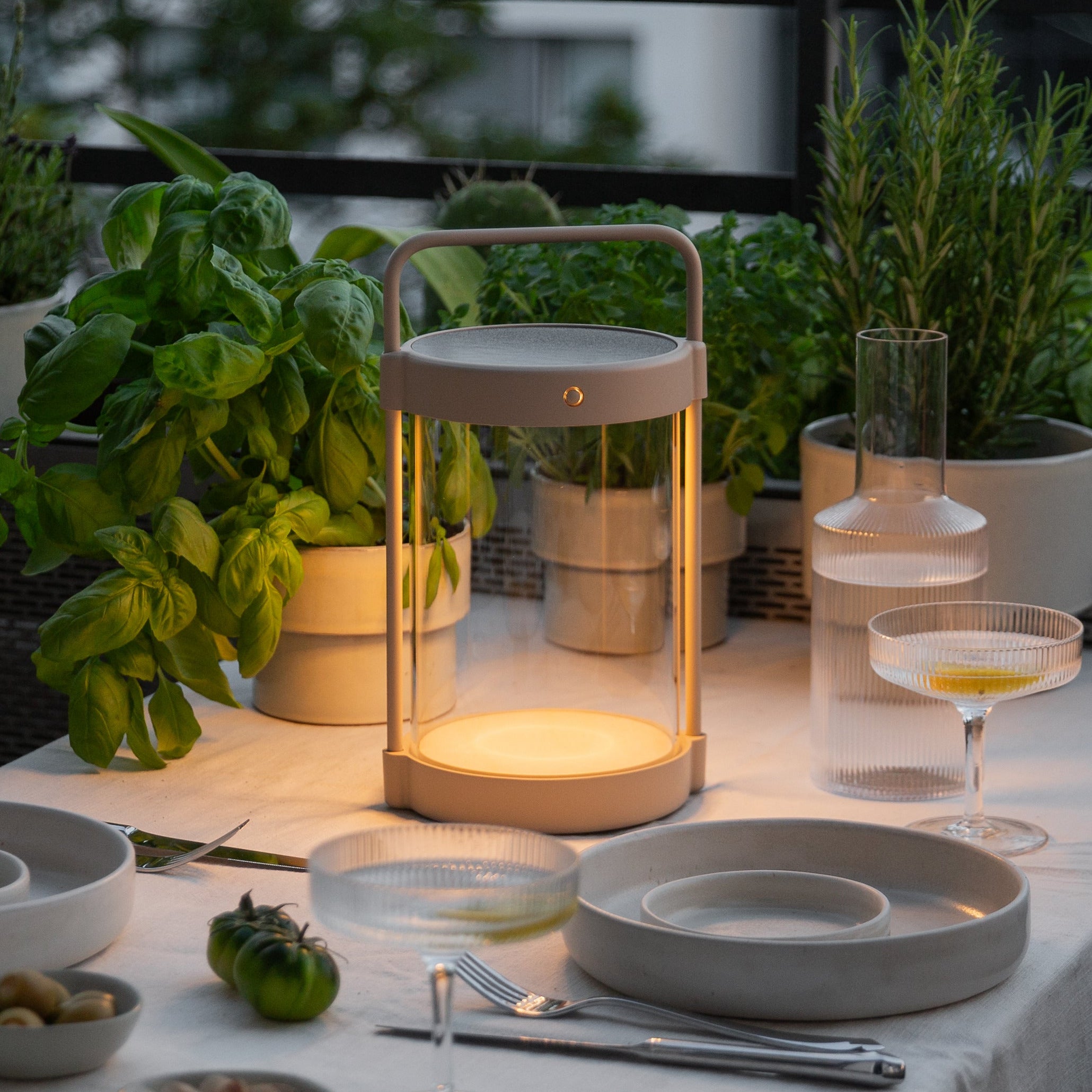 Moderne Caia Solarlampe in Beige beim Einsatz auf gedecktem Balkontisch mit warmweißen Licht – stimmungsvolle, kabellose LED-Außenbeleuchtung bei Abenddämmerung