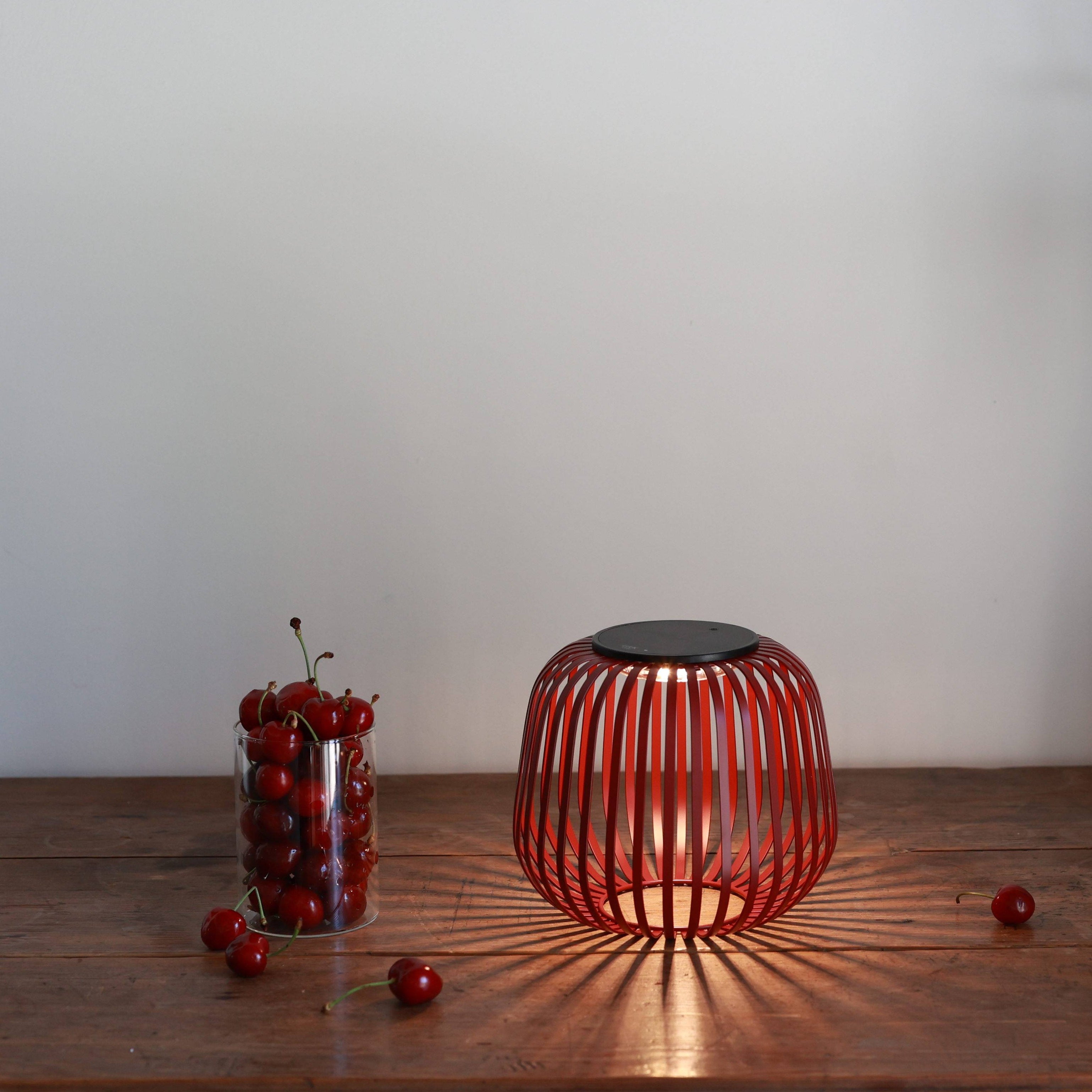 Dekorative LUUK Solarlampe in dunkelrot mit Schattenwurf auf Holztisch mit Kirschen und Rosen in Vase 