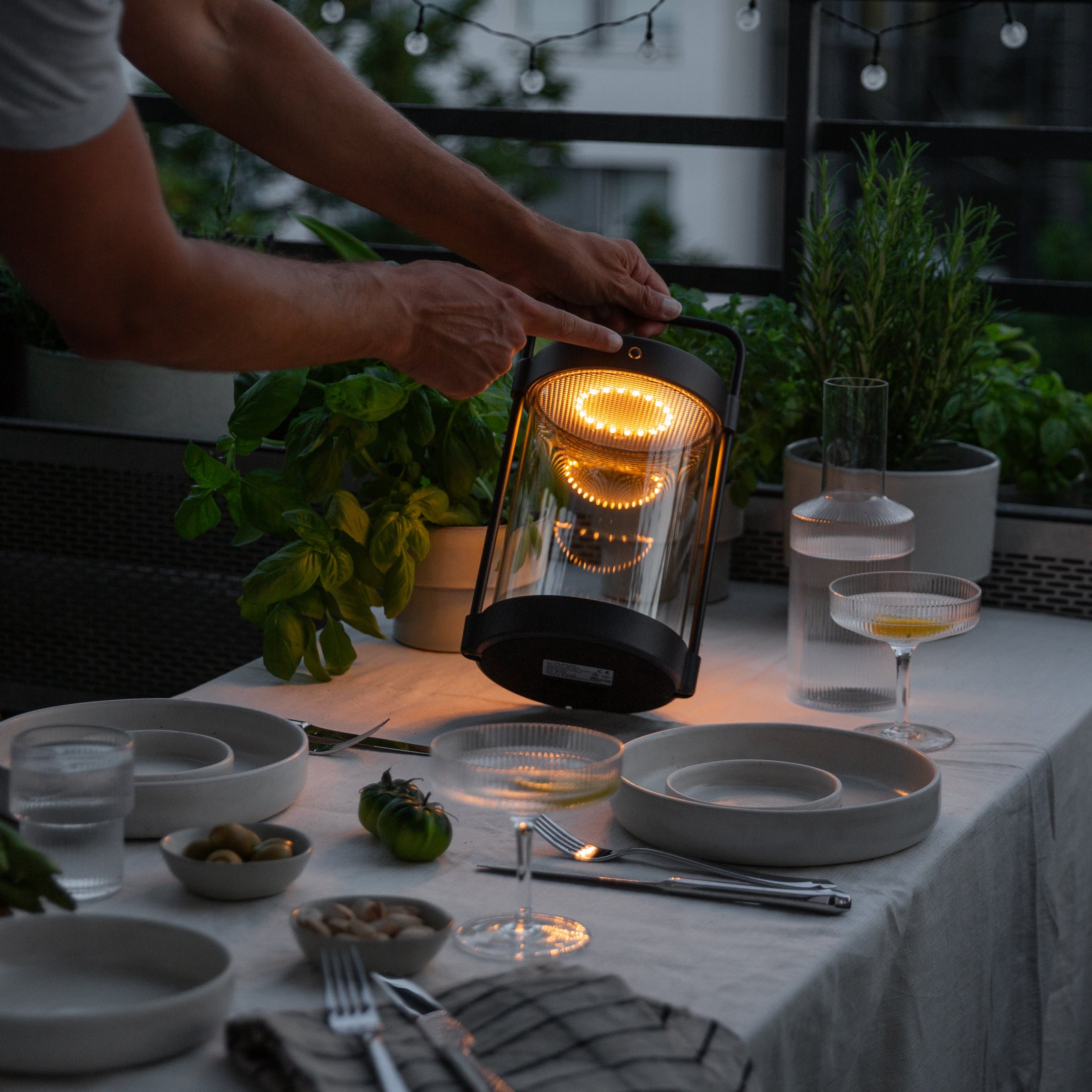 Caia Outdoorlaterne ohne Kabel in Dunkelheit auf gedecktem Tisch mit warmweißem Licht auf Balkon im Sommer