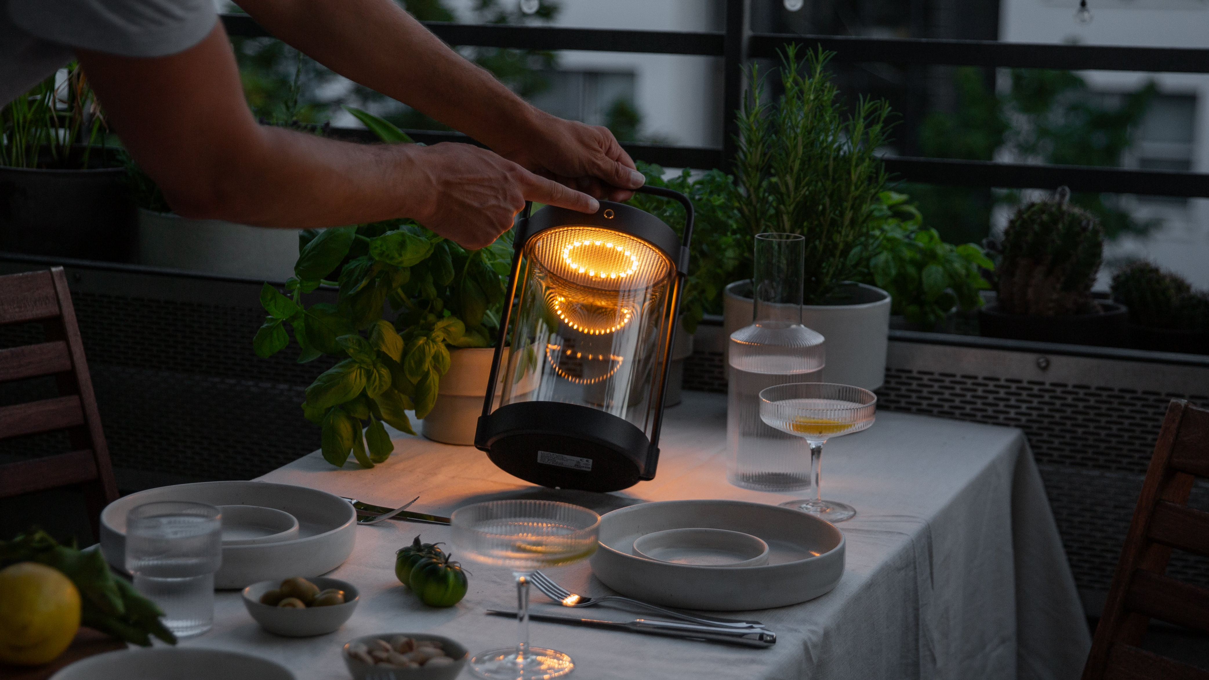Caia Outdoorlaterne ohne Kabel in Dunkelheit auf gedecktem Tisch mit warmweißem Licht auf Balkon im Sommer