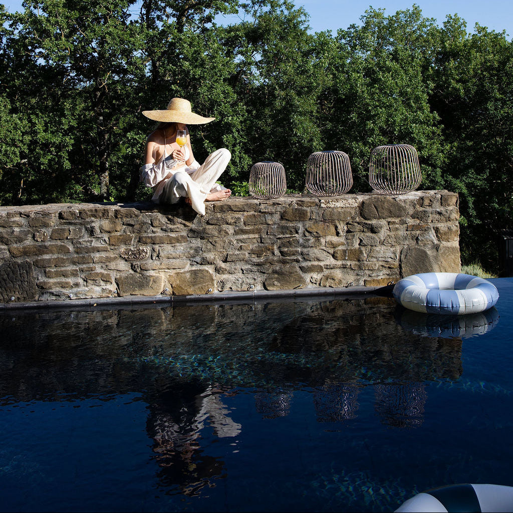 Ein Stimmungsbild im Sommer mit einer Frau auf einer Steinmauer oberhalb des Pools neben drei Solis Laternen