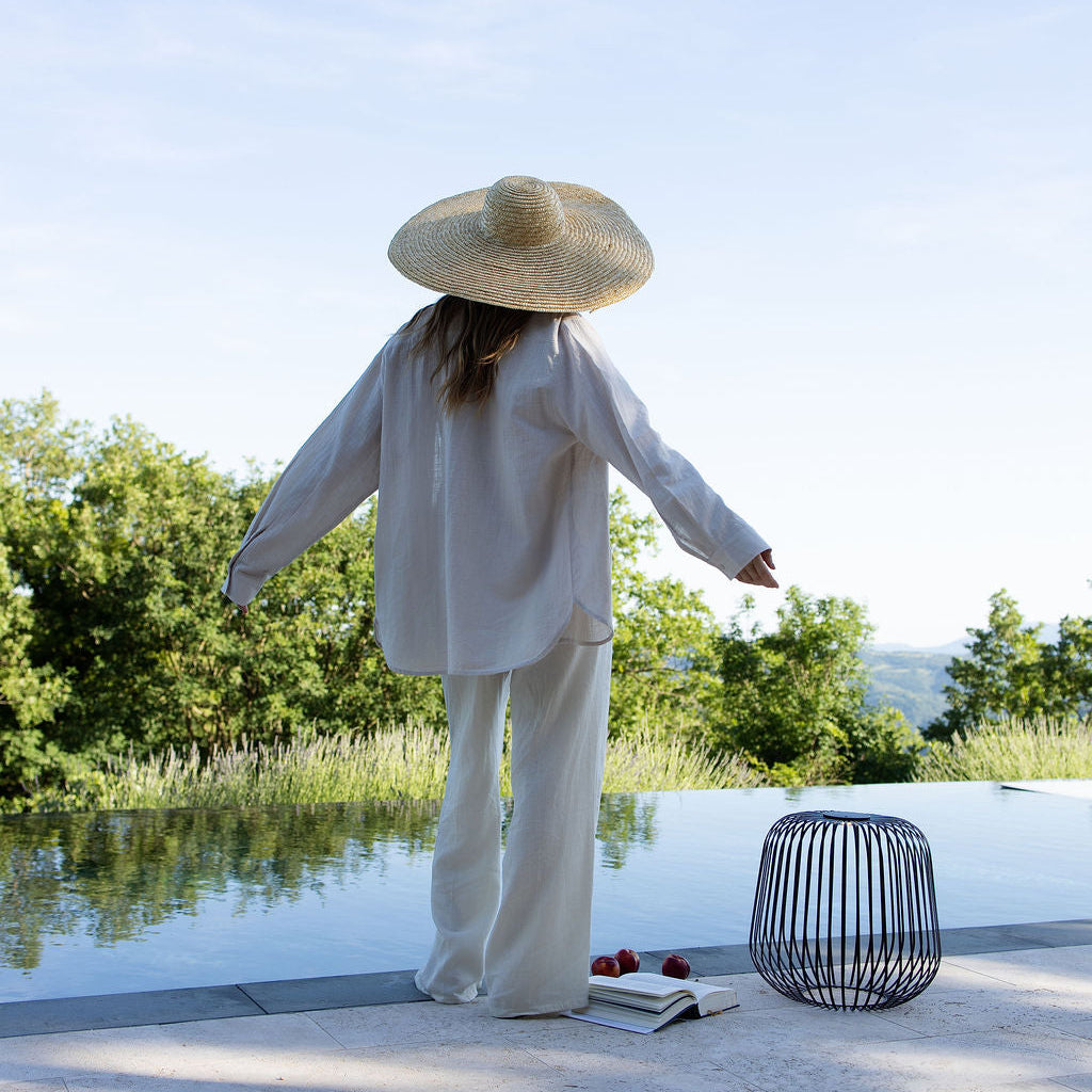 Eine Frau im Sommerlook steht am Pool und geniesst einen warmen Sommertag mit frischen Früchten, einem Buch und der Solis Laterne als schönes Stimmungslicht.