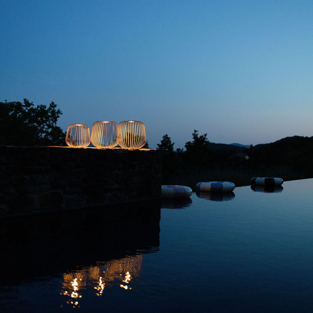 Ein Stimmungsbild der drei Solis Laternen in der Grösse L-XL und XXL bei Nacht an einem Outdoorpol im Garten mit Spiegelung im Wasser