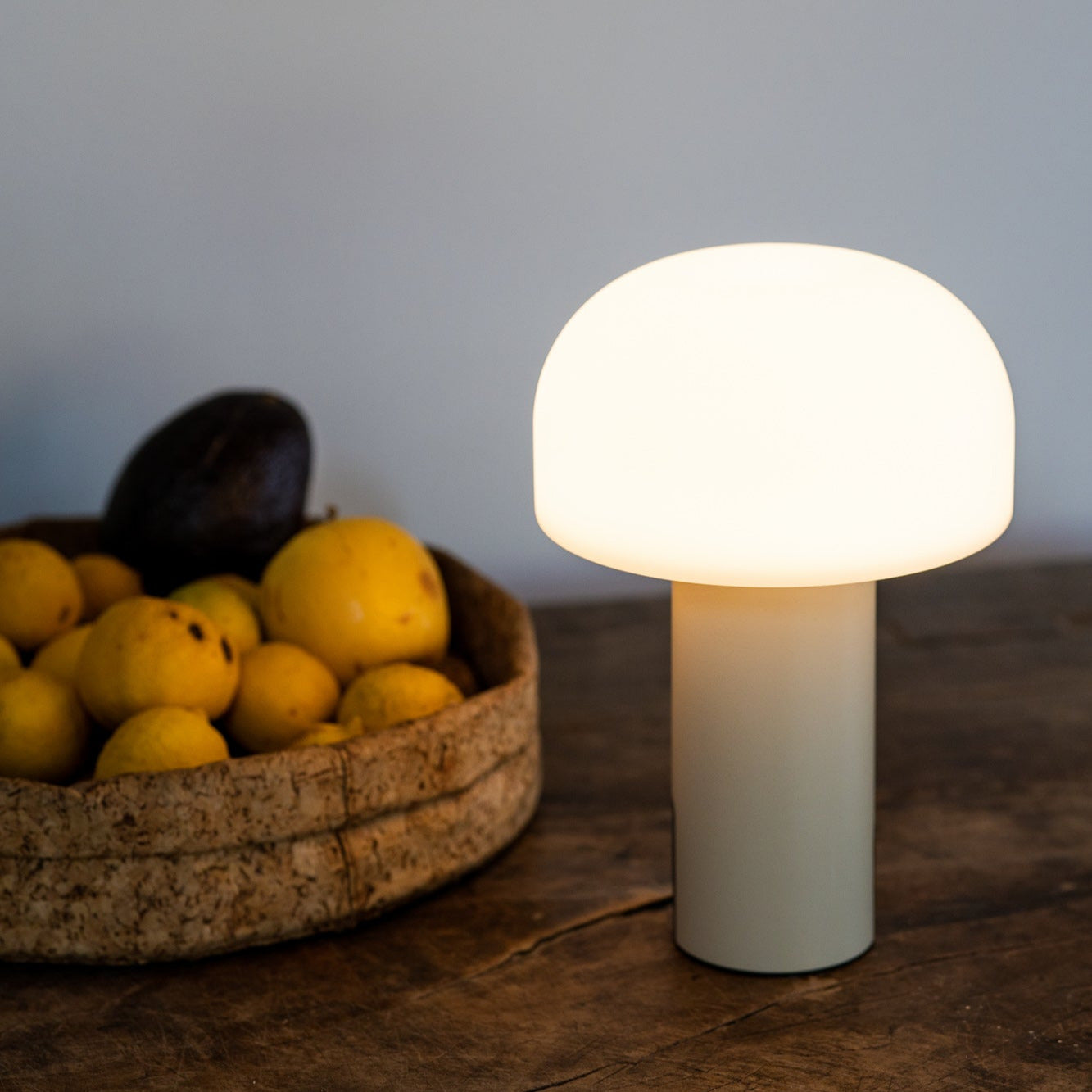 Noa LED-Tischleuchte mit pilzförmigem Schirm in Cremeweiß auf rustikalem Holztisch neben Zitronen, ideal als sanfte Lichtquelle für Esszimmer, Küche oder Sideboard.