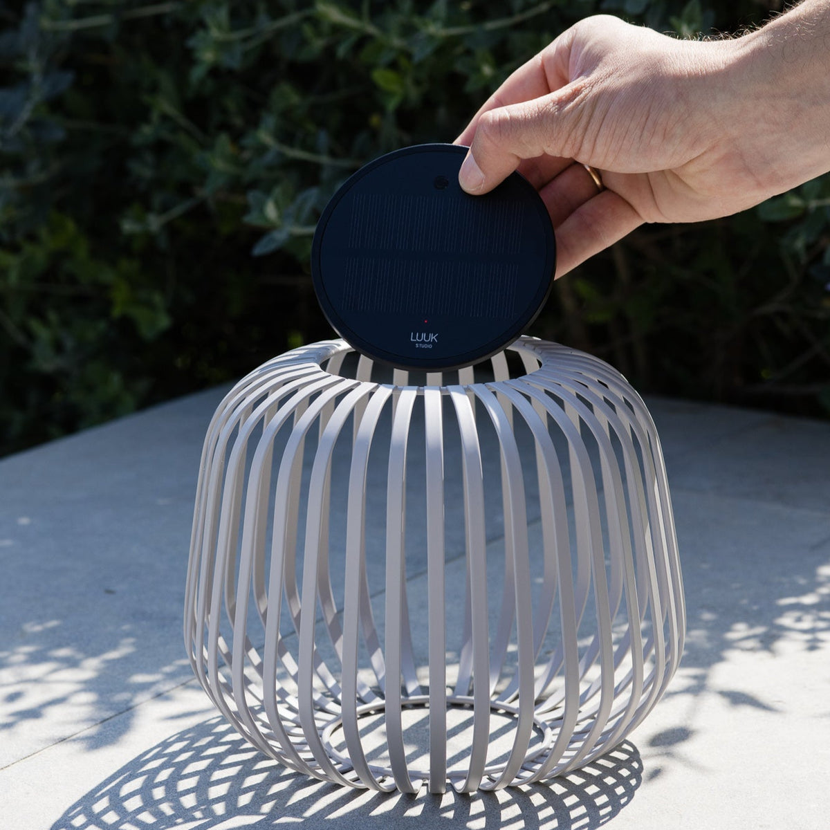 Hand setzt herausnehmbares Solarmodul mit USB-C Anschluss von LUUK Studio auf LED-Lampe mit Metallrahmen im Outdoor-Bereich